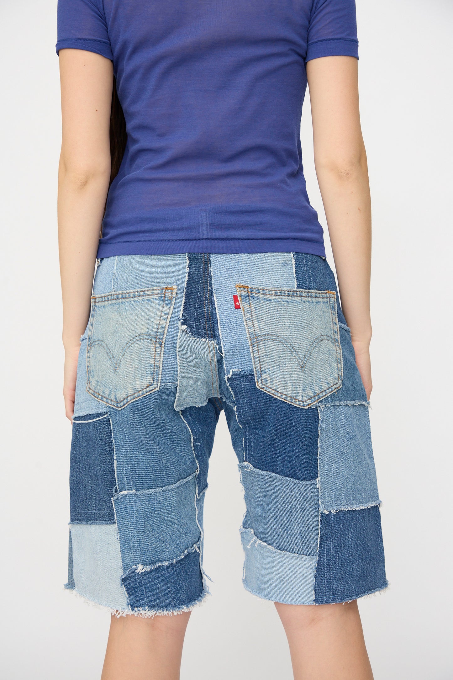 Someone wearing a purple shirt and B Sides Rework Madras Short in Vintage Indigo stands facing away from the camera against a plain background.