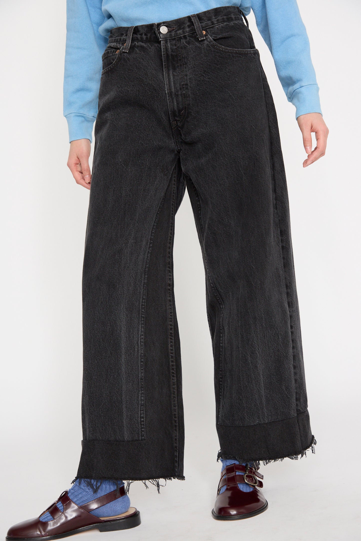 A person wearing a blue sweater, B Sides Reworked Culotte in Vintage Black, and burgundy loafers stands against a plain background, seen from below the waist.