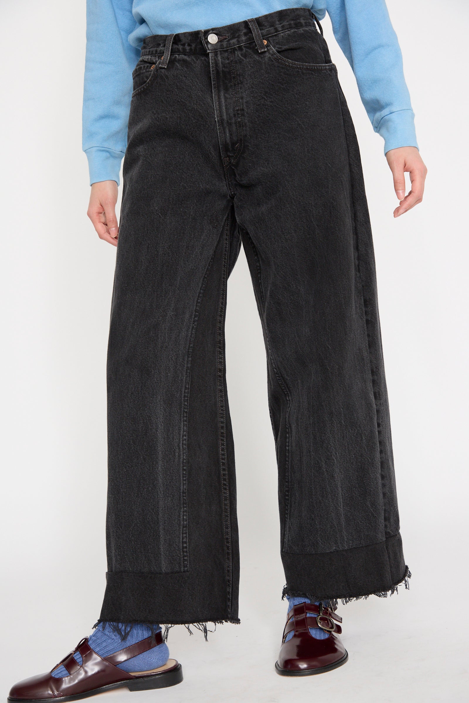 A person wearing a blue sweater, B Sides Reworked Culotte in Vintage Black, and burgundy loafers stands against a plain background, seen from below the waist.