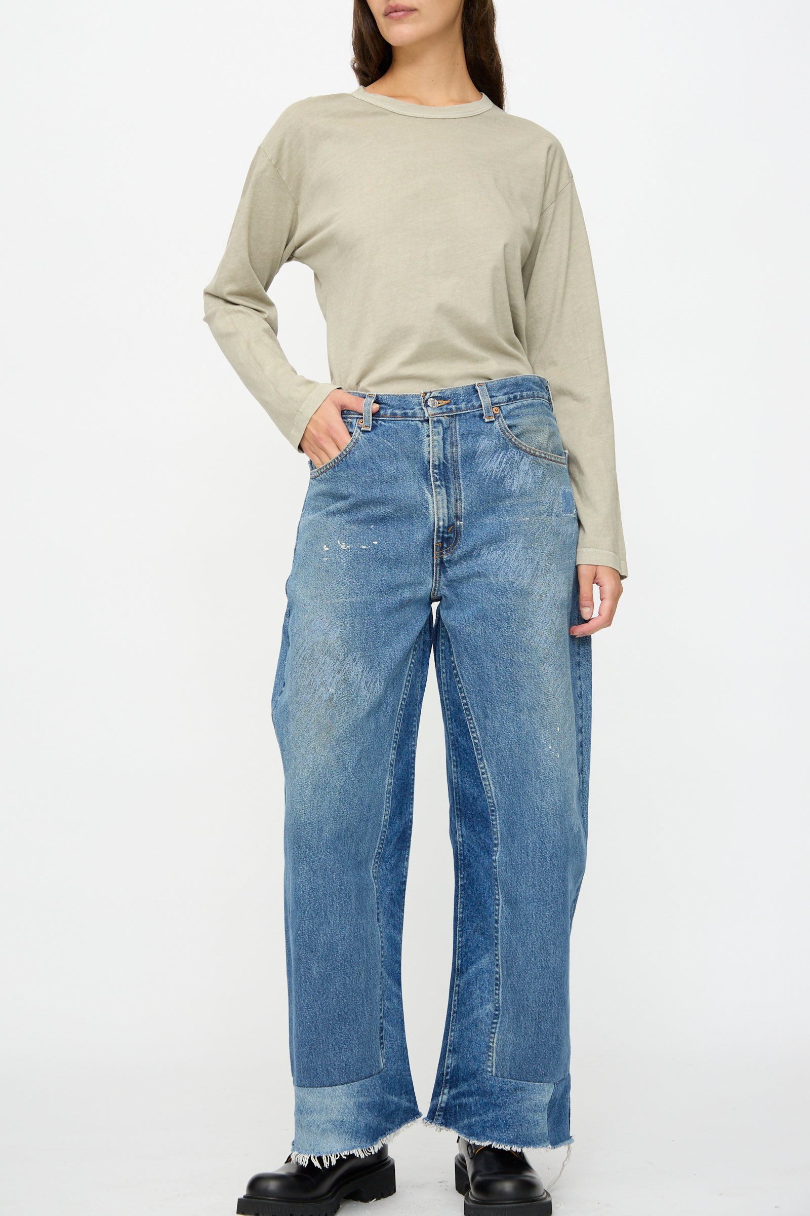 A person stands against a plain background wearing a beige long-sleeve shirt, black shoes, and B Sides Reworked Culotte in Vintage Indigo—wide-leg denim pants with frayed hems.