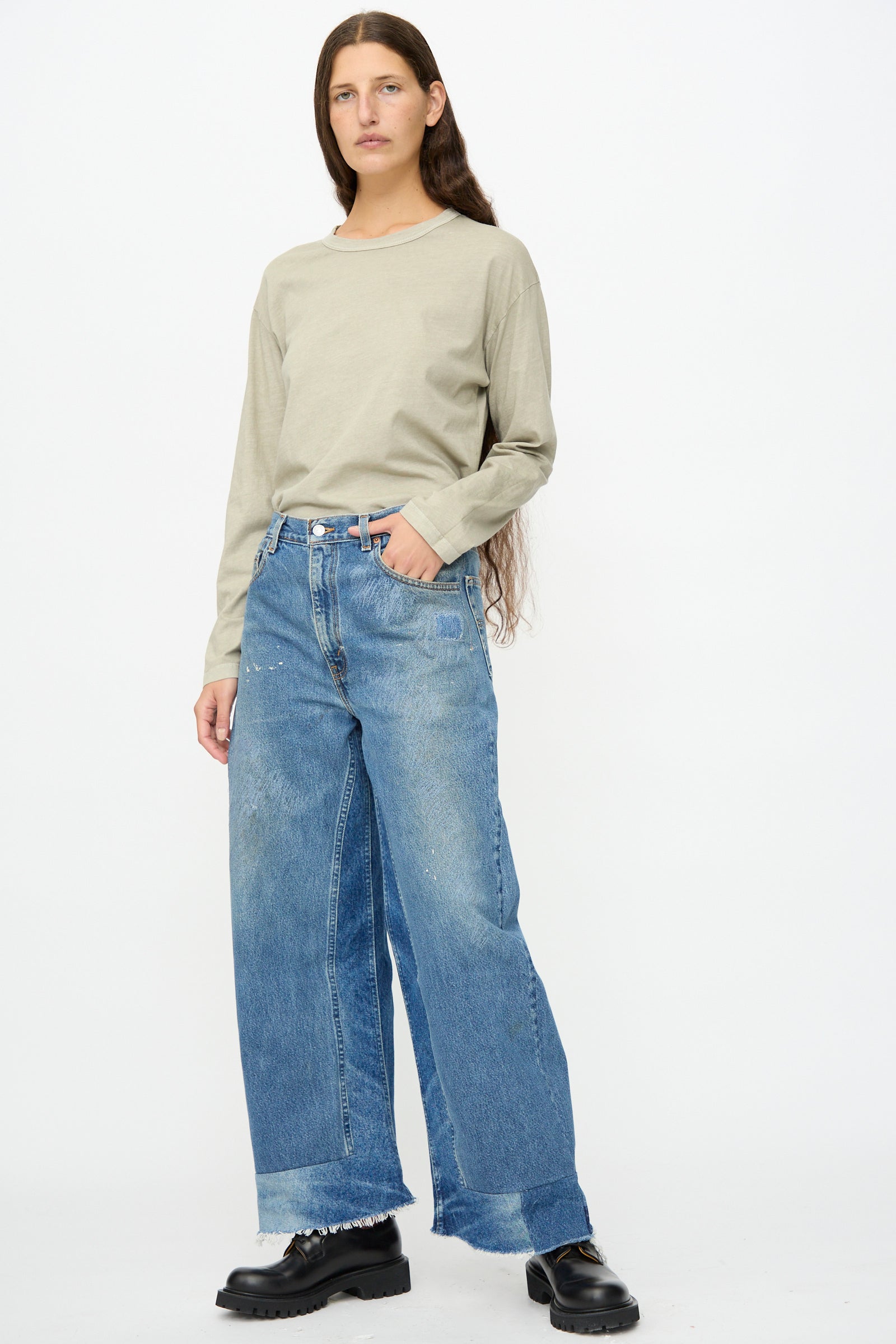Person stands against a plain background, wearing a long-sleeve beige shirt, B Sides Reworked Culotte in Vintage Indigo with wide legs and frayed hems, and black platform shoes.