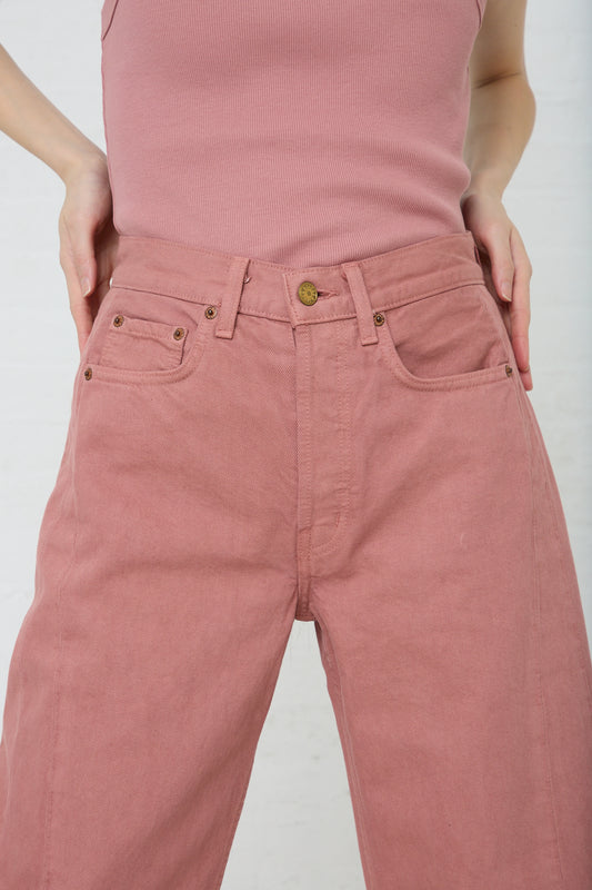 A person wearing a Slim Lasso in Zinnia Overdye tucked into rose-colored vintage denim jeans, standing with hands in back pockets against a white background.