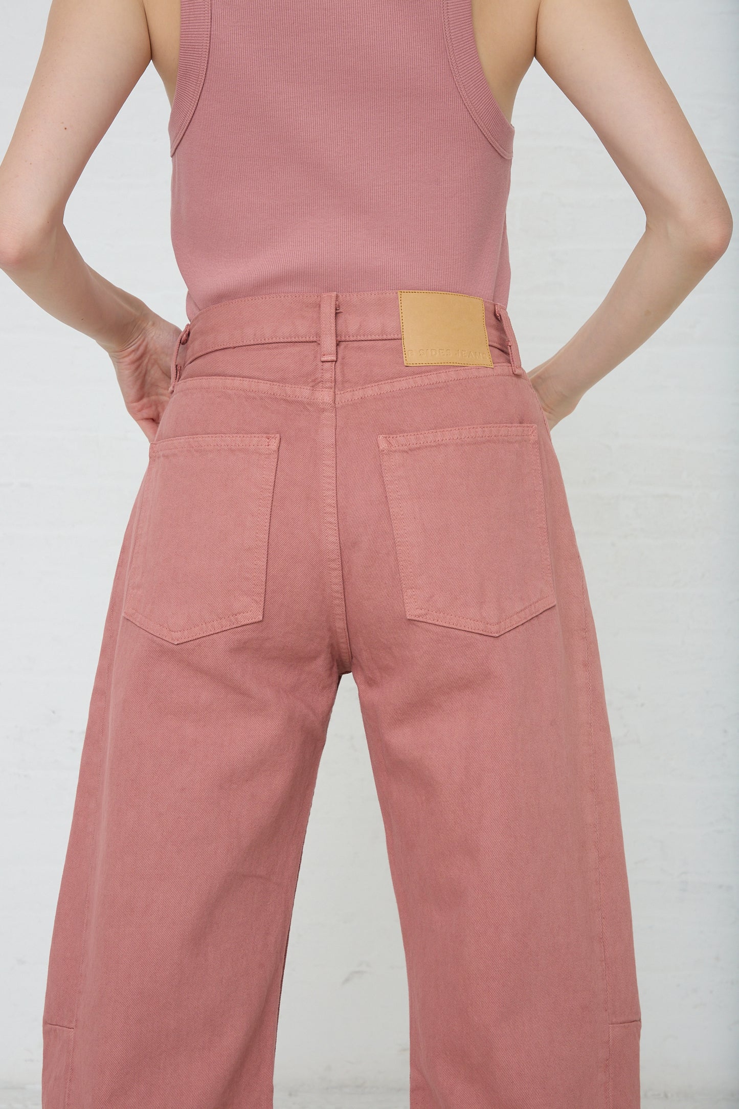 A person standing with hands on their hips wearing pink, vintage high-waisted Slim Lasso in Zinnia Overdye pants by B Sides.