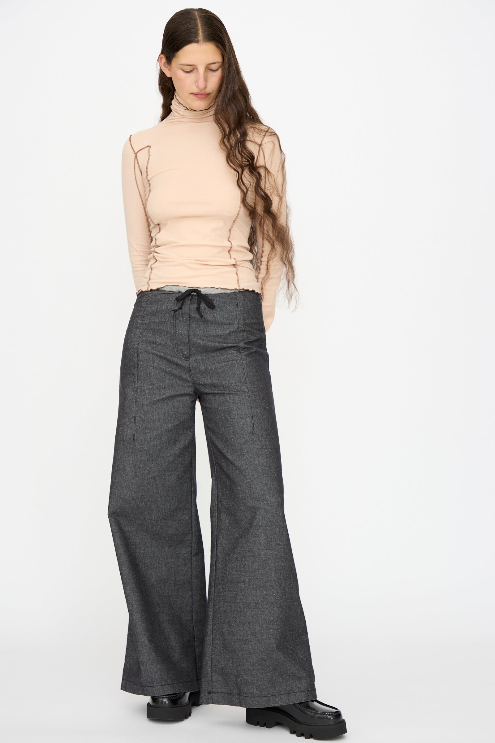 A person stands against a plain background wearing a beige long-sleeve turtleneck top and Baserange Arthur Loose Pants in Black.