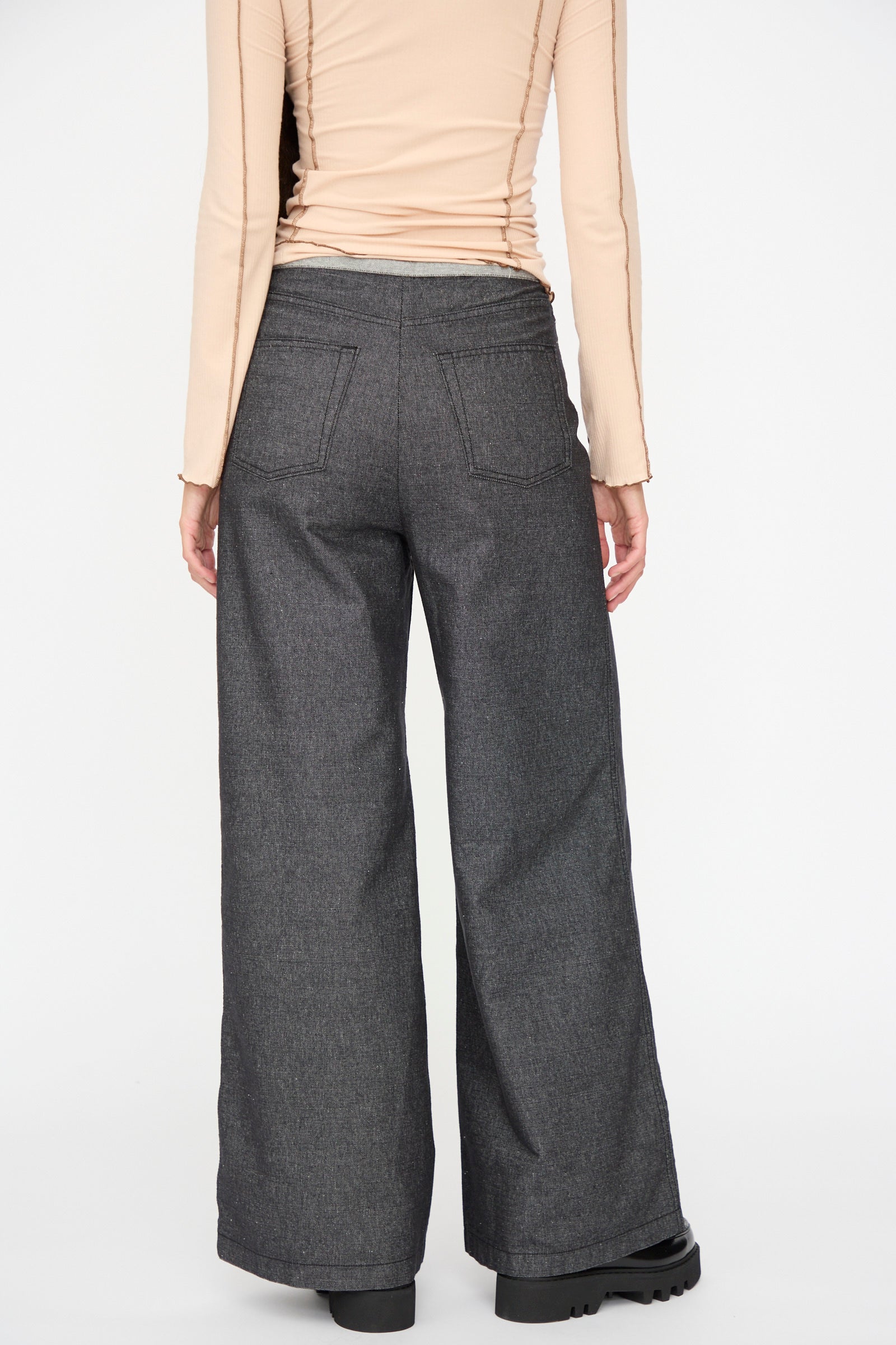 A person stands with their back to the camera, wearing Baserange's Arthur Loose Pants in Black and a beige long-sleeve top against a plain background.