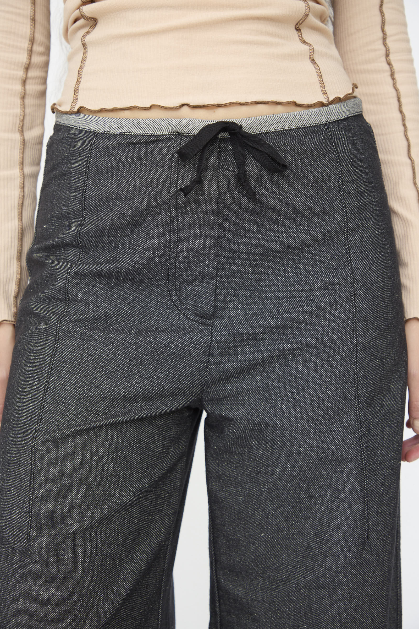 Someone wearing Baserange Arthur Loose Pants in Black paired with a beige long-sleeve top with exposed seams and subtle flared mid-waist jeans.
