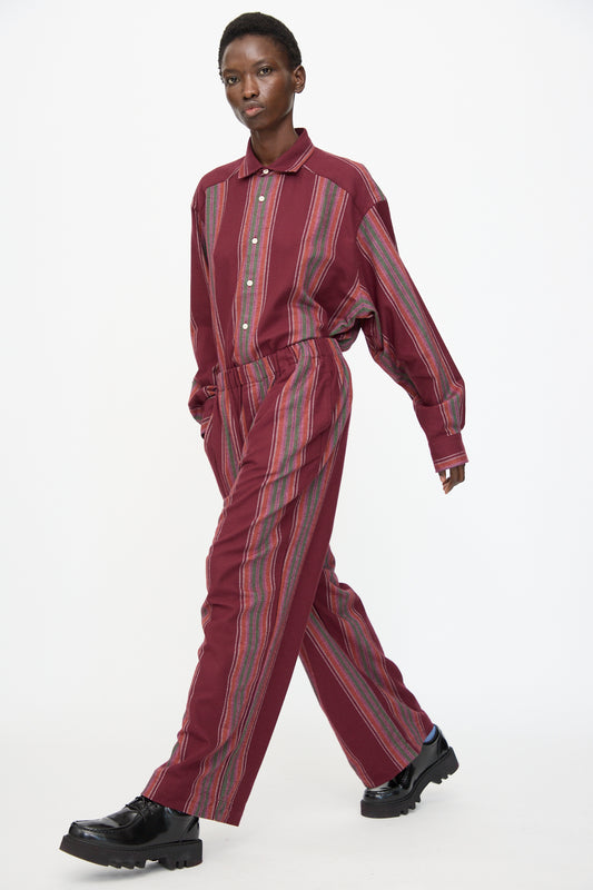 A person walks forward against a plain white background, wearing Baserange's Claude Pants in Maroon Stripe.