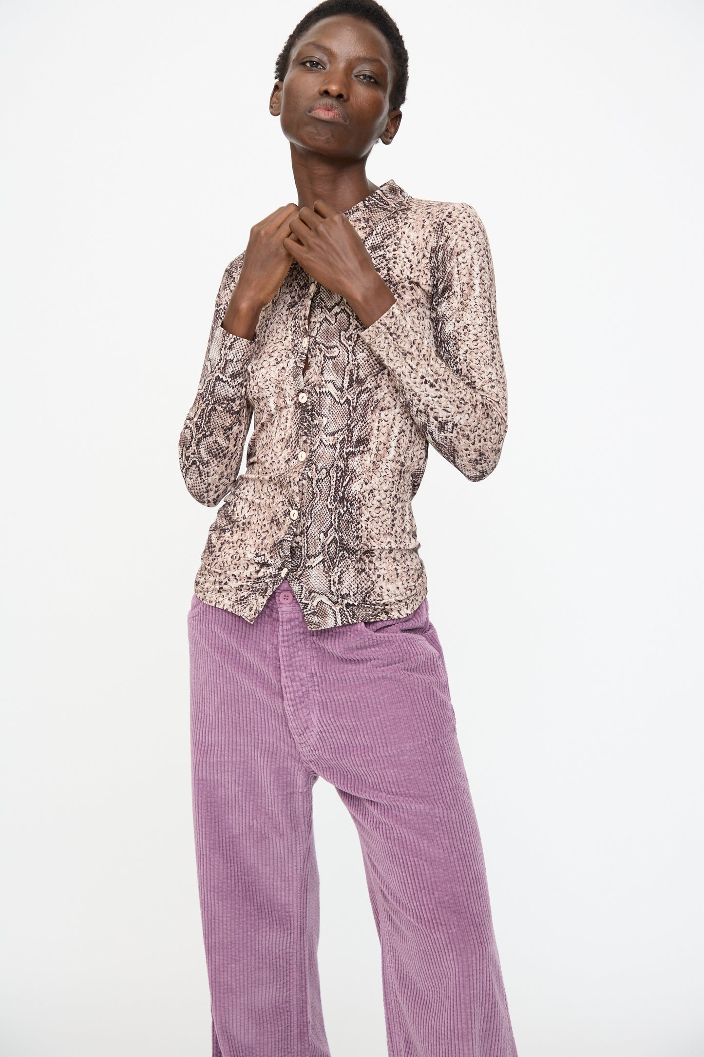 A person wears the Baserange Cosme Shirt in Snake, a slim-fit, long-sleeve top, paired with high-waisted light purple corduroy pants and stands against a plain white background.