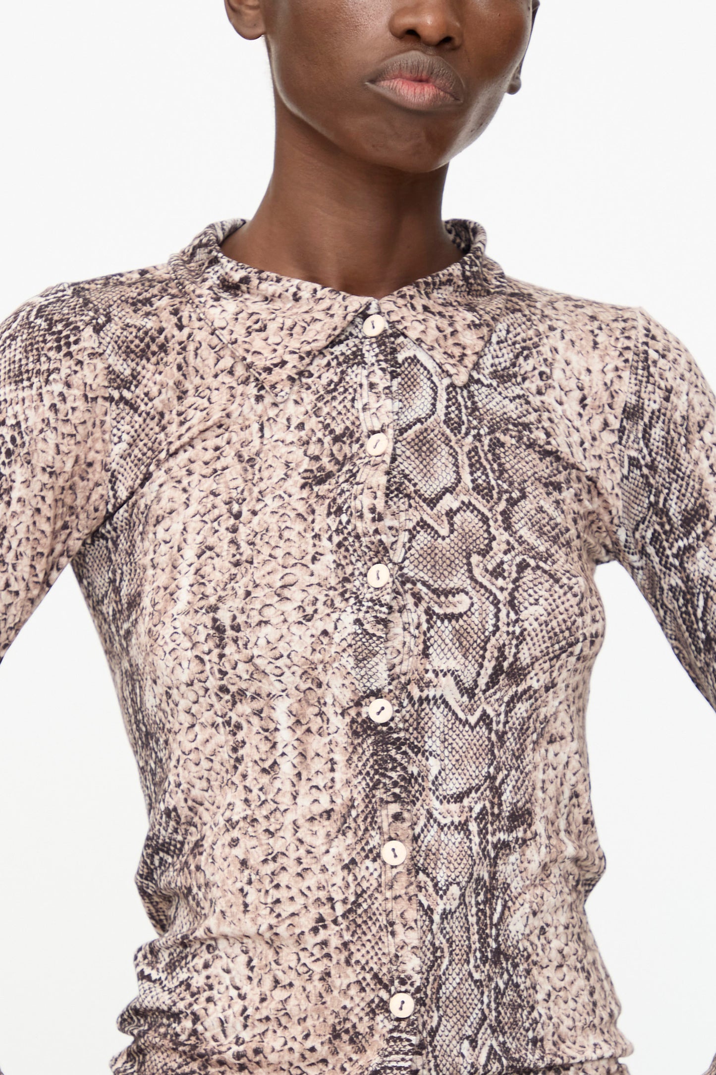 A person wearing the Baserange Cosme Shirt in Snake, a slim fit, long-sleeve top featuring a beige and brown snake print pattern.