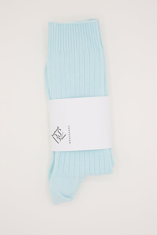 A pair of folded Baserange Cotton Rib Overankle Socks in Lagoon Blue with packaging on a white background.