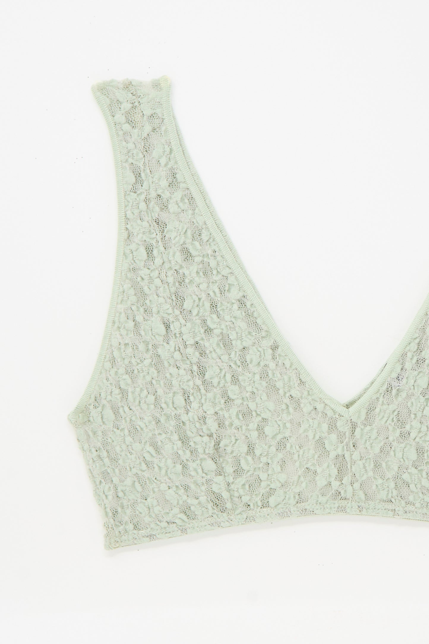 The Crescent Bra in Conta Green by Baserange is a light green lace V-neck bra with a deep neckline, crafted from delicate fabric and displayed on a plain white background.