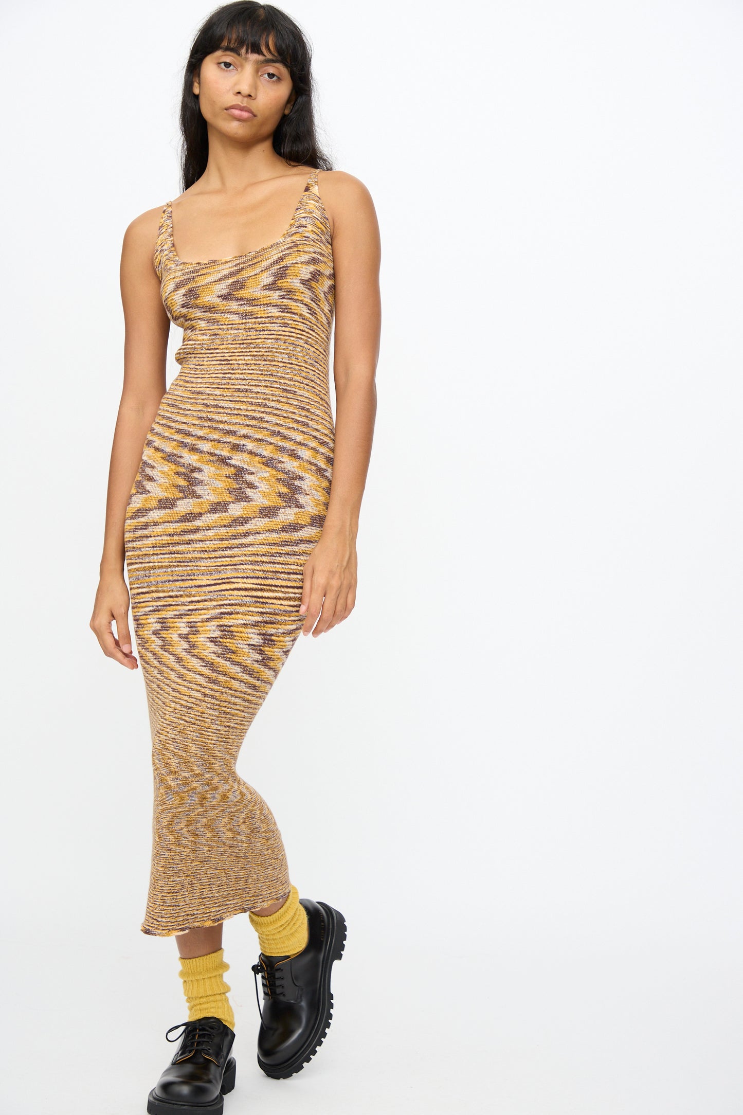 A woman wears the Baserange Flute Dress in Brown Melange, paired with yellow socks and black boots, standing against a plain white background.