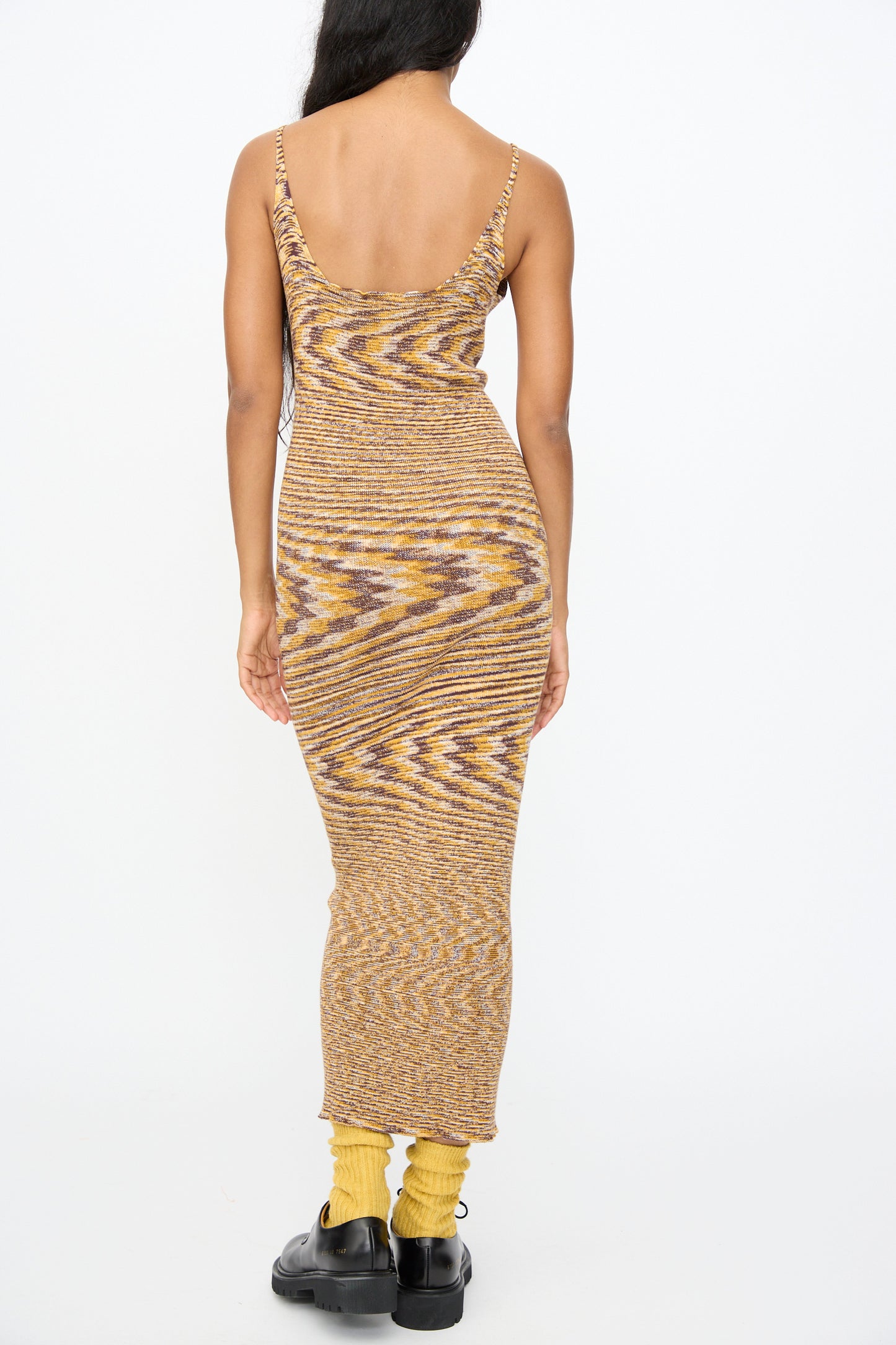 A person wearing the Baserange Flute Dress in Brown Melange with yellow socks and black shoes is shown from the back against a plain background.