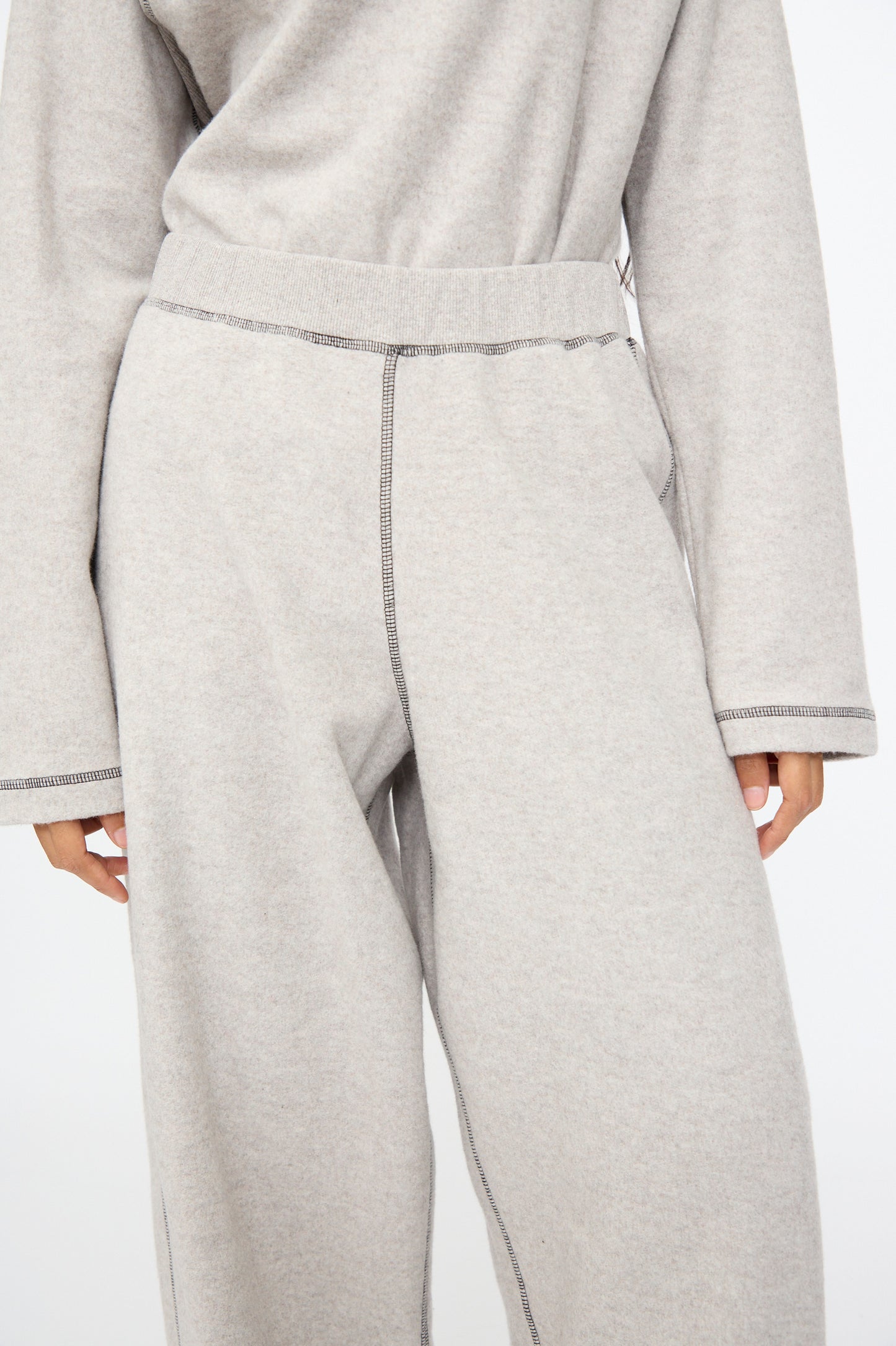 Model wears Baserange Fold Sweatpant in Grey Melange, a relaxed fit, wide-leg style with visible seam stitching, paired with a light gray long-sleeve top; shown from shoulders to mid-thigh.