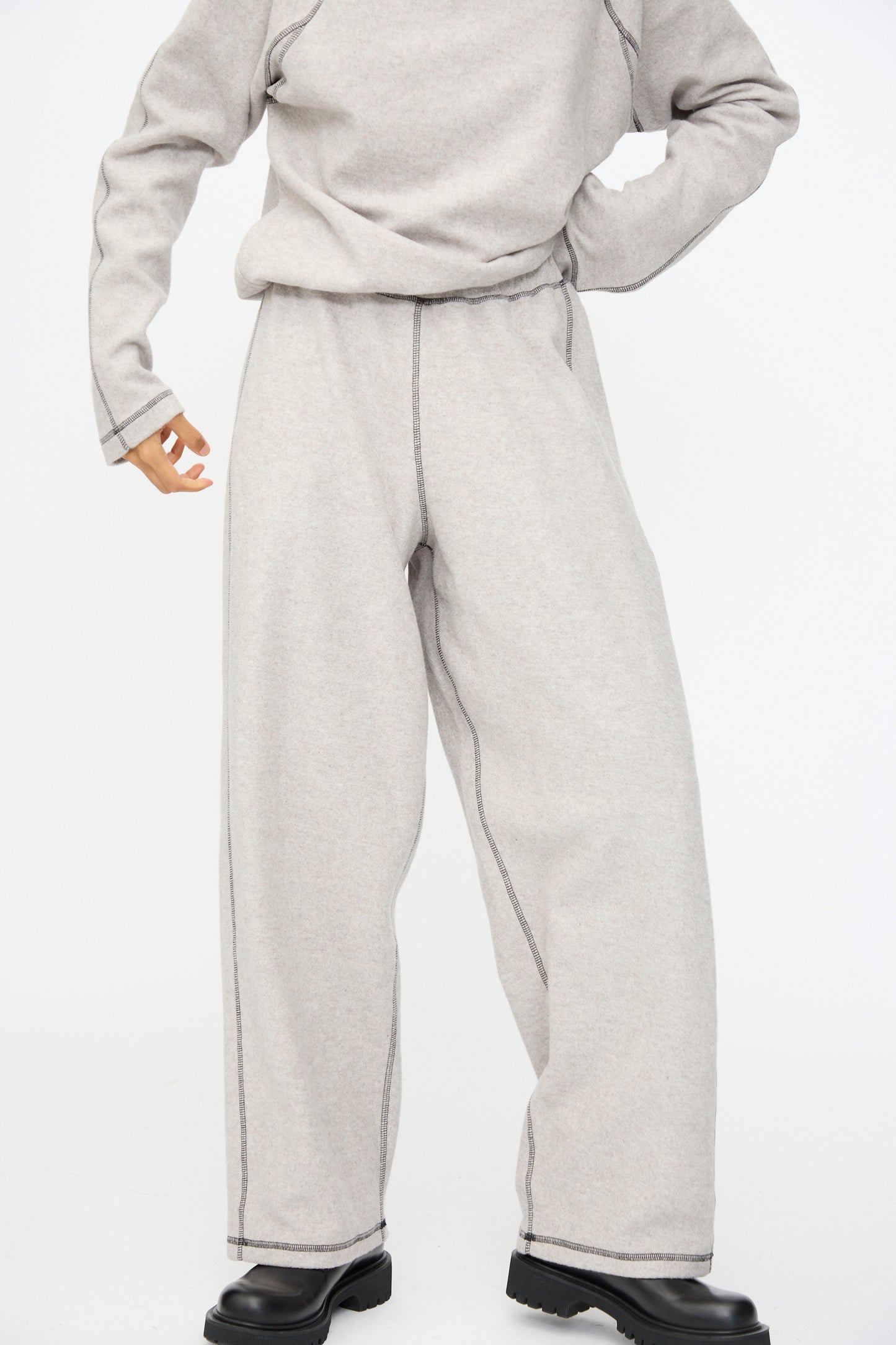 A person wears the Baserange Fold Sweatpant in Grey Melange with a relaxed fit light gray sweatshirt and black shoes, standing against a plain white background.