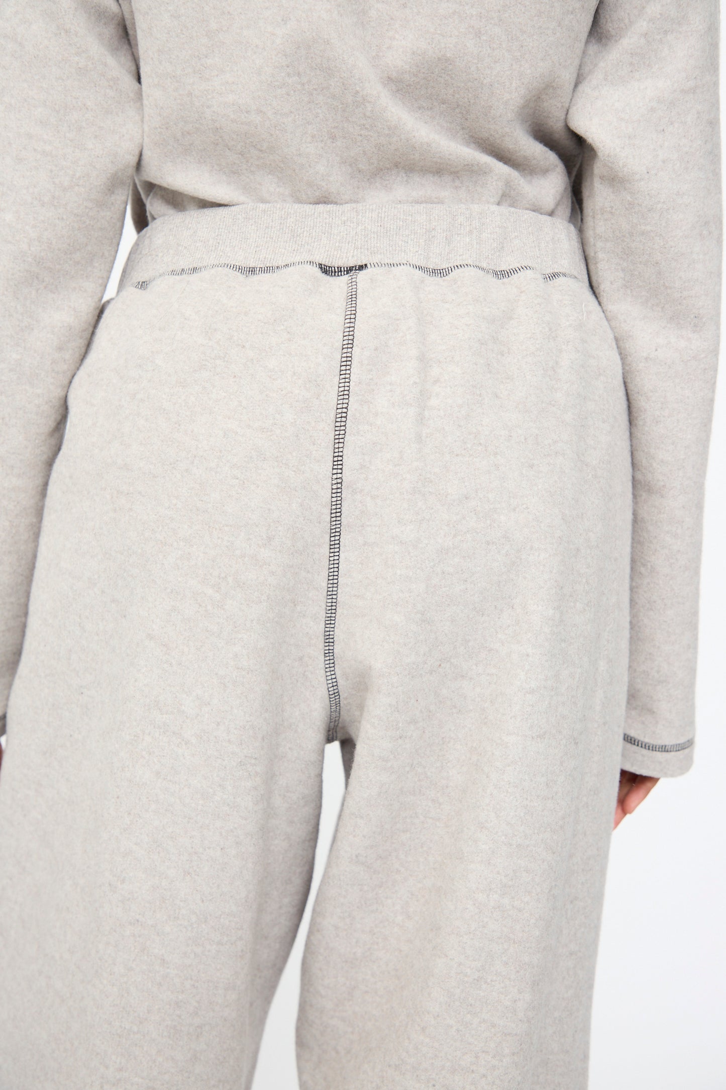 Person wearing Baserange Fold Sweatpant in Grey Melange, featuring a relaxed fit and visible dark stitching on the waistband and center seam, photographed from the back at waist level.