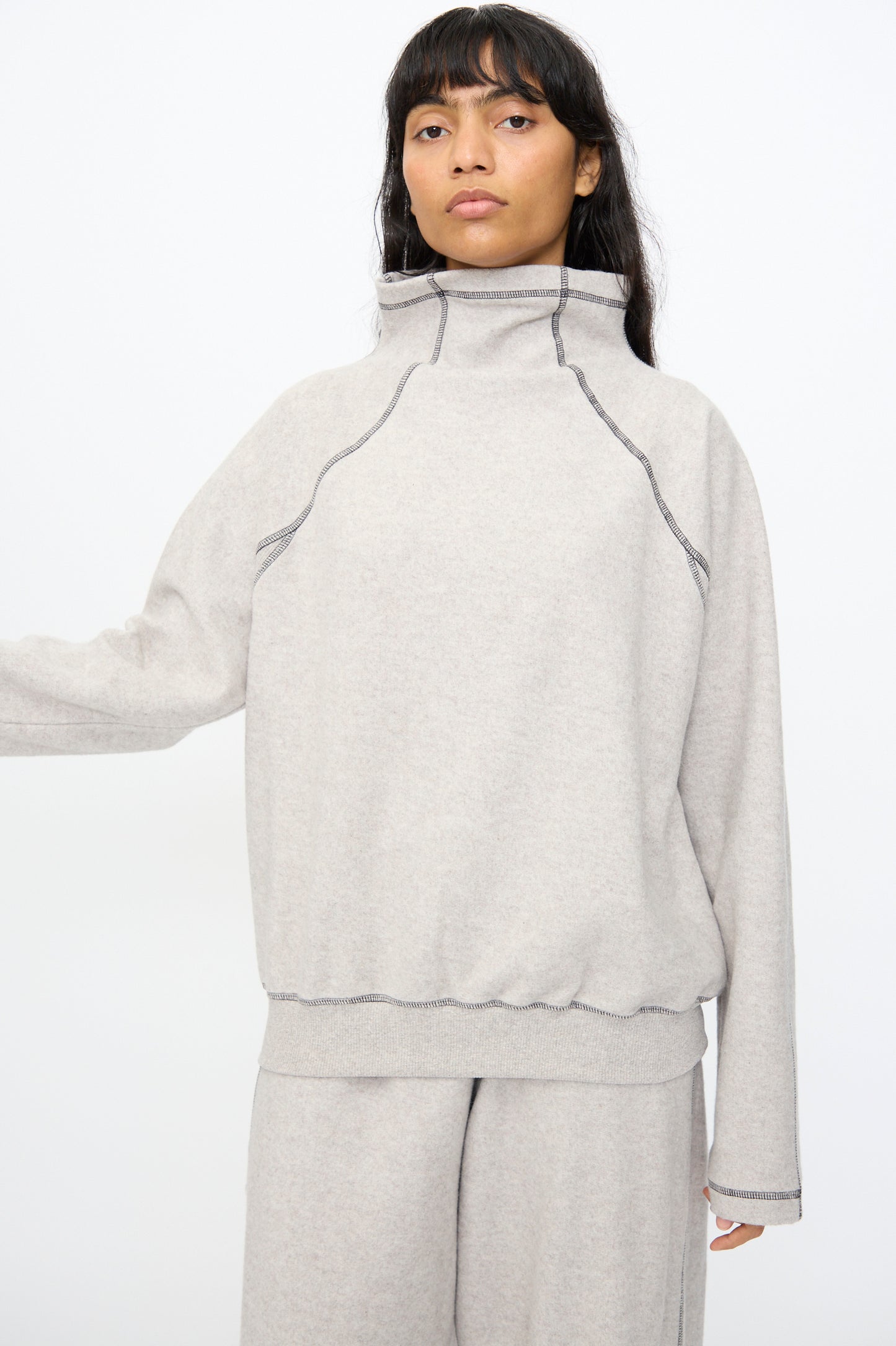 A person wearing the Baserange Fold Turtleneck in Grey Melange, an oversized recycled cotton sweatshirt, with matching pants, stands against a plain white background.