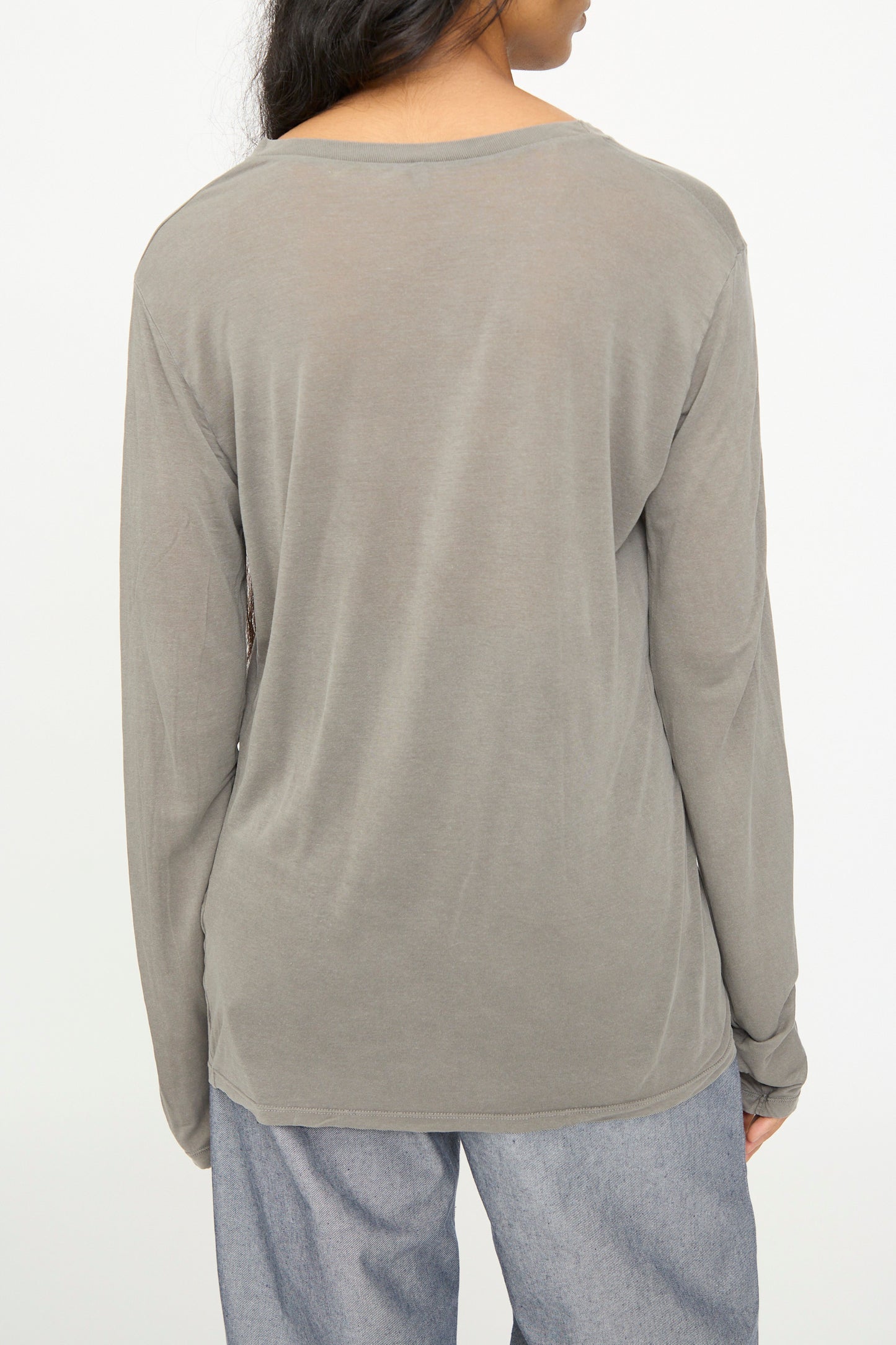 A person wearing the Baserange Long Sleeve Tee in Gilda Grey and light blue pants, photographed from behind against a plain light background.