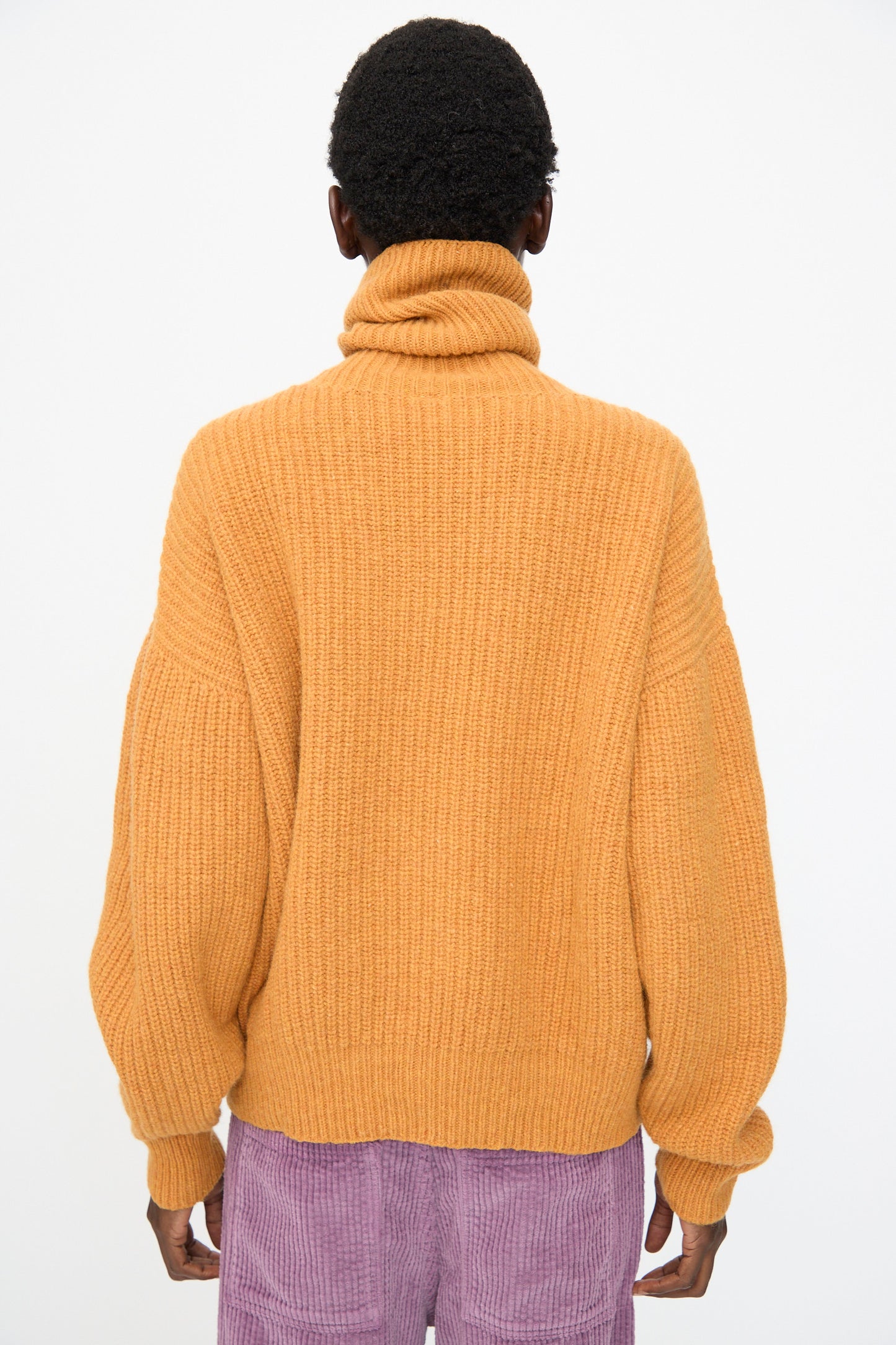 Person facing away from the camera wearing the Baserange Mea Turtleneck in Clair Orange against a plain white background.