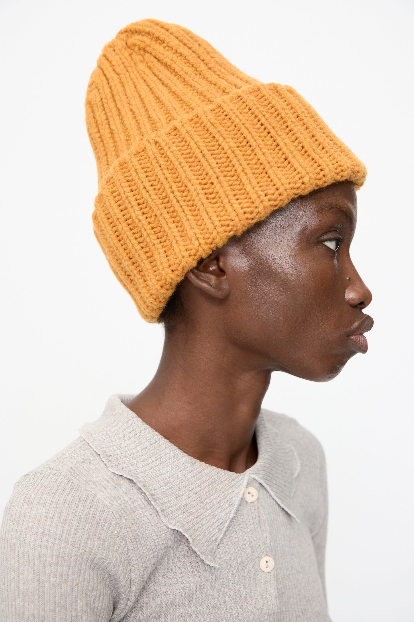 A person in profile wears the Baserange Mea Beanie in Clair Orange and a light gray collared sweater, set against a plain white background.
