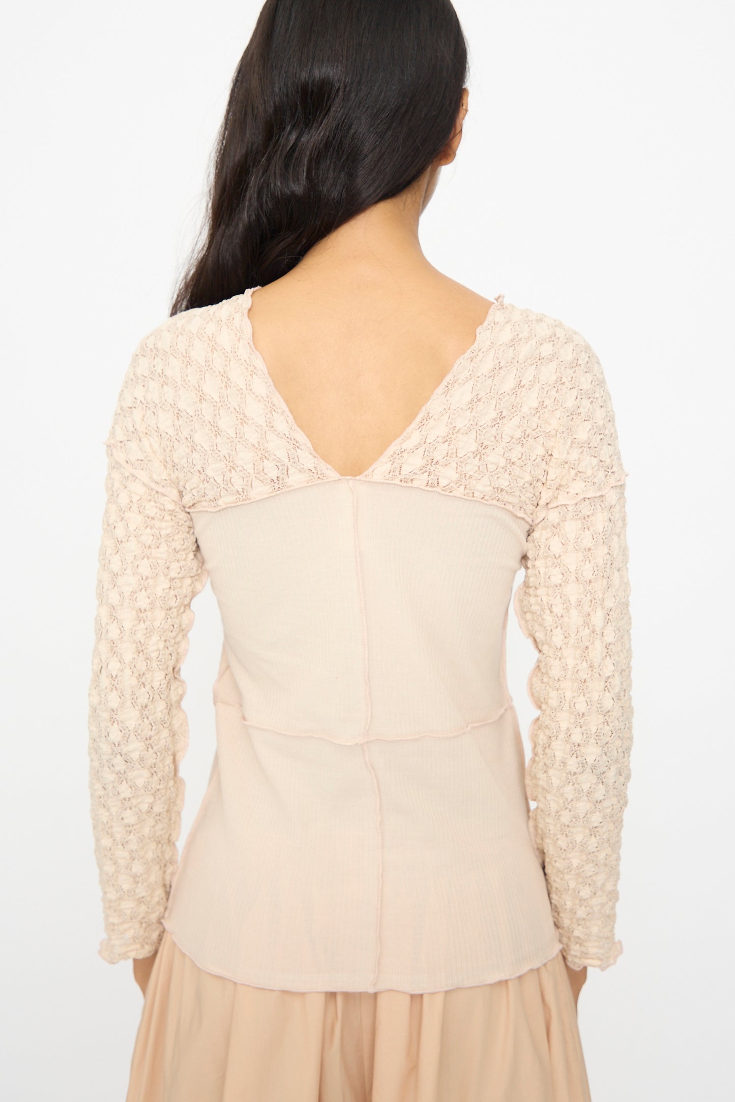 A woman with long dark hair, seen from behind, wears the Baserange Nehru Long Sleeve Tee in Dylan Beige against a plain background.