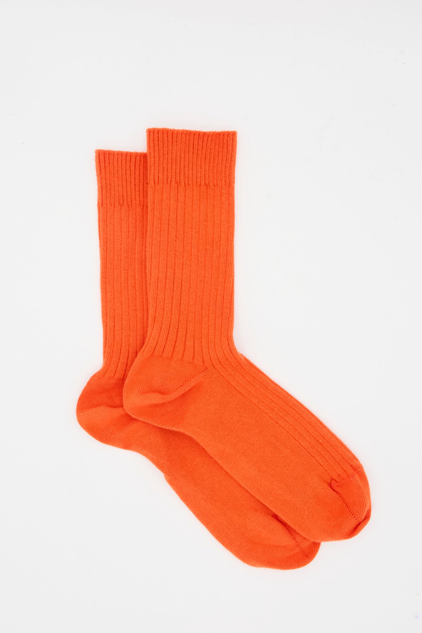 A pair of Baserange Rib Overankle Socks in Chiral Red, crafted from ribbed organic cotton and made in France, laid flat on a white background.