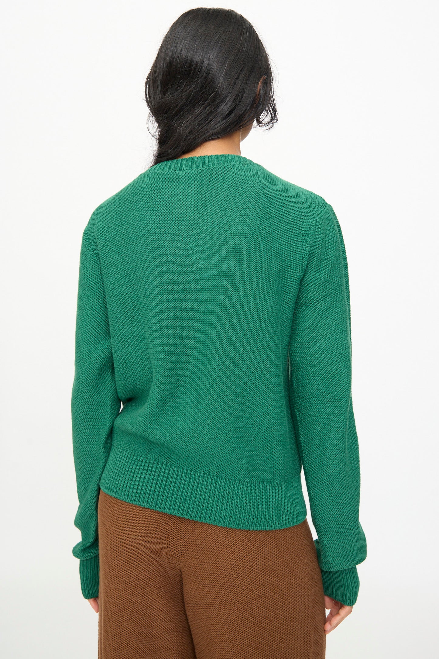 A person with dark hair, shown from the back against a plain light background, is wearing the Baserange Tier Cardigan in Calla Green paired with brown pants.