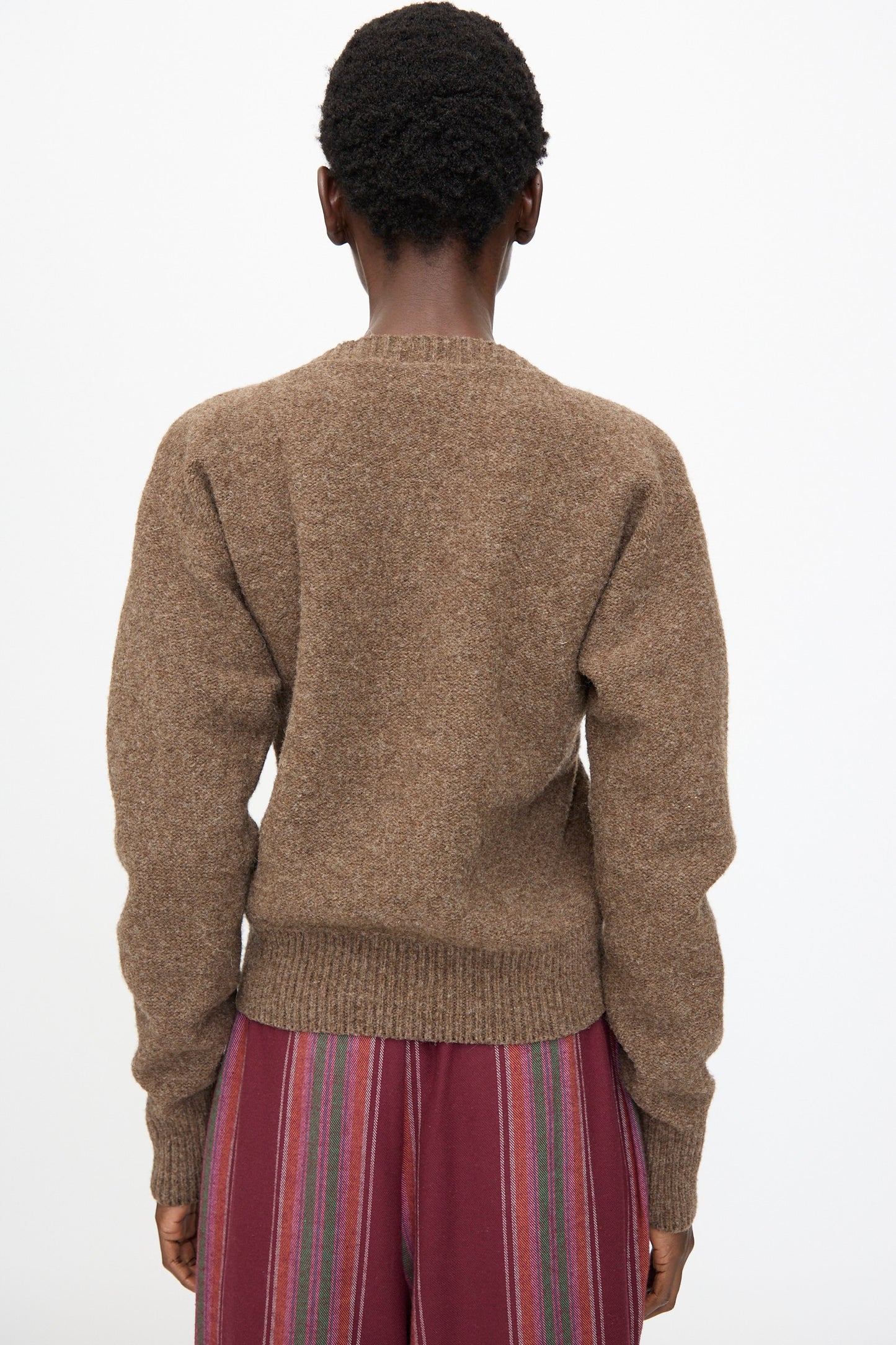 A person is shown from behind wearing the Baserange Tier Sweater in Burel Brown and maroon striped pants, standing against a plain white background.