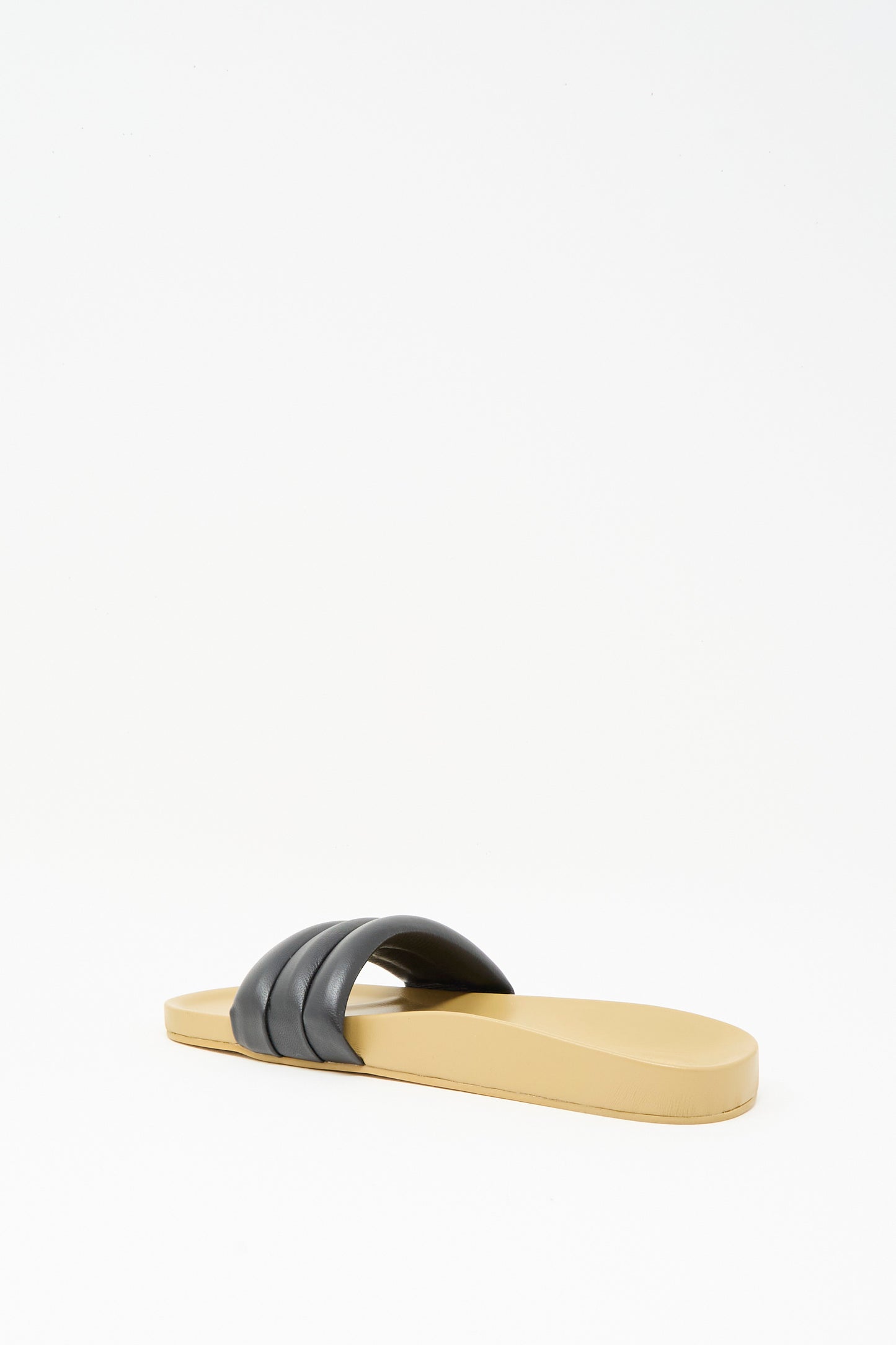 The Beatrice Valenzuela Classic Sandalia in Black is a beige handcrafted slide sandal featuring a flat sole and a wide black strap, showcased against a plain white background.