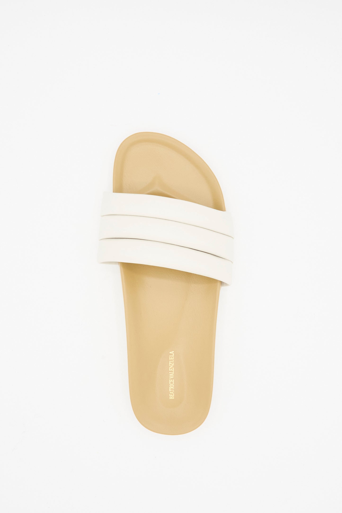 The Classic Sandalia in Shell by Beatrice Valenzuela is a handcrafted beige slide sandal with two wide white straps, shown from above on a plain white background.