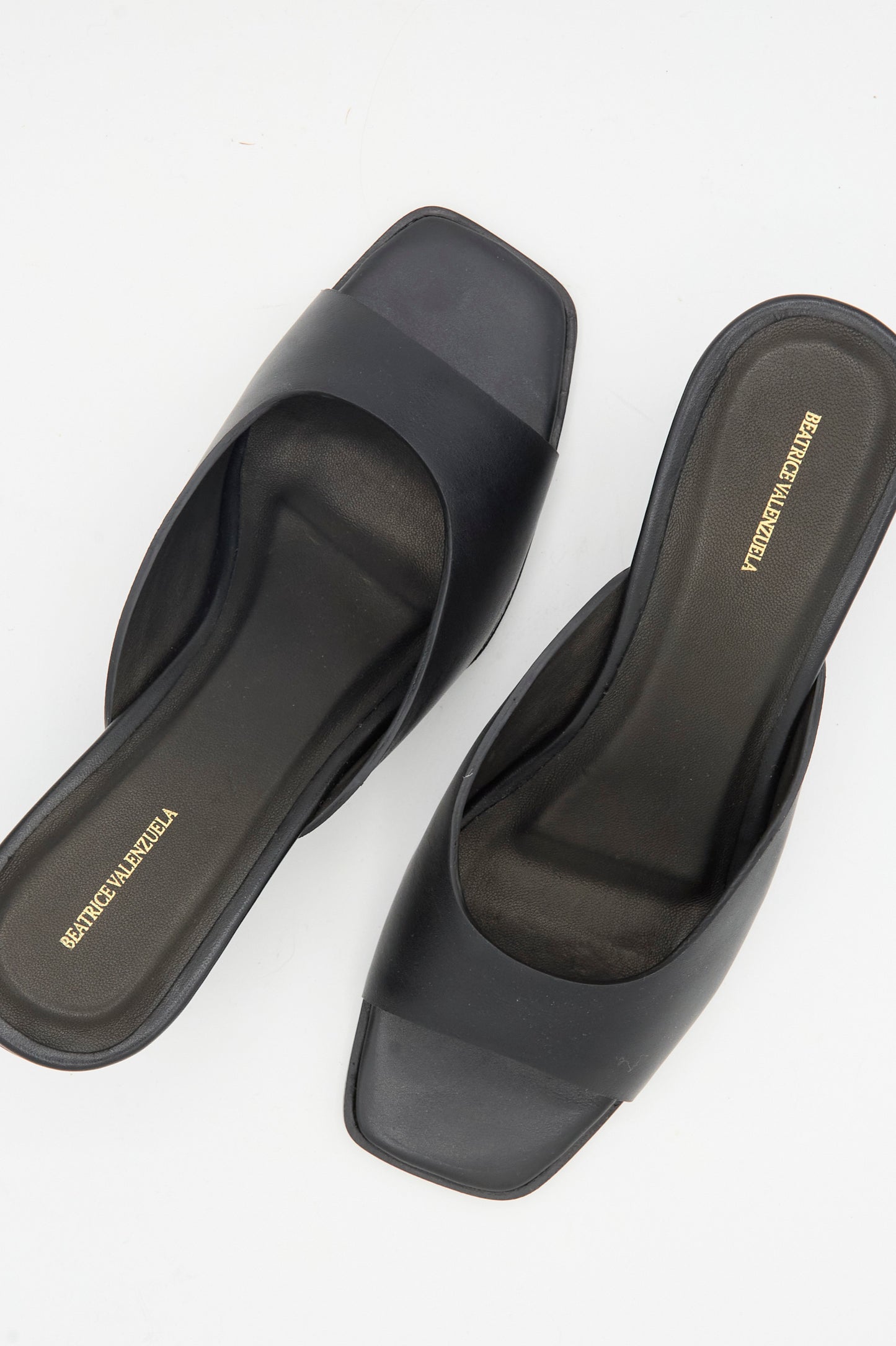 The Moderna Wedge Sandal in Black by Beatrice Valenzuela features open toes, square fronts, and a simple strap design made from Nappa cow leather, shown against a white background.