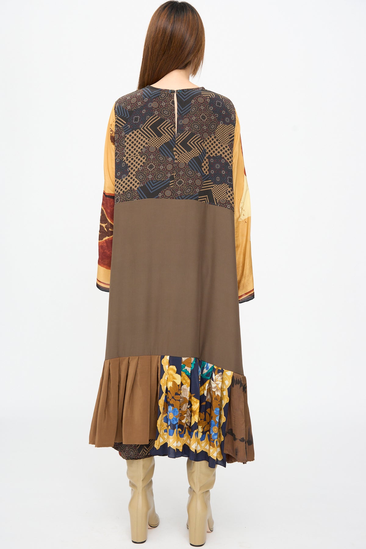 A person viewed from behind wearing the Bettina Bakdal Hannah Dress in Ise Gropius, a knee-length vintage silk dress with geometric and floral patterns in brown, gold, and blue, paired with tan boots.