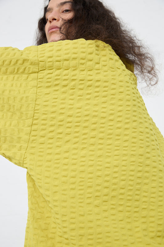 A person in a Black Crane Cotton Seersucker Chelsea Collar Shirt in Turmeric is turning their head to the side, partially obscuring their face.