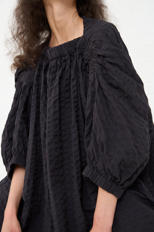 A woman wearing a black cotton seersucker sack dress in ink black with puff sleeves, cropped at the shoulders by Black Crane.