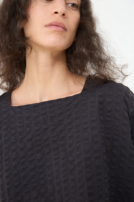 A woman with curly hair wearing a textured Black Crane Cotton Seersucker Square Neck Top in Ink Black, looking to the side.
