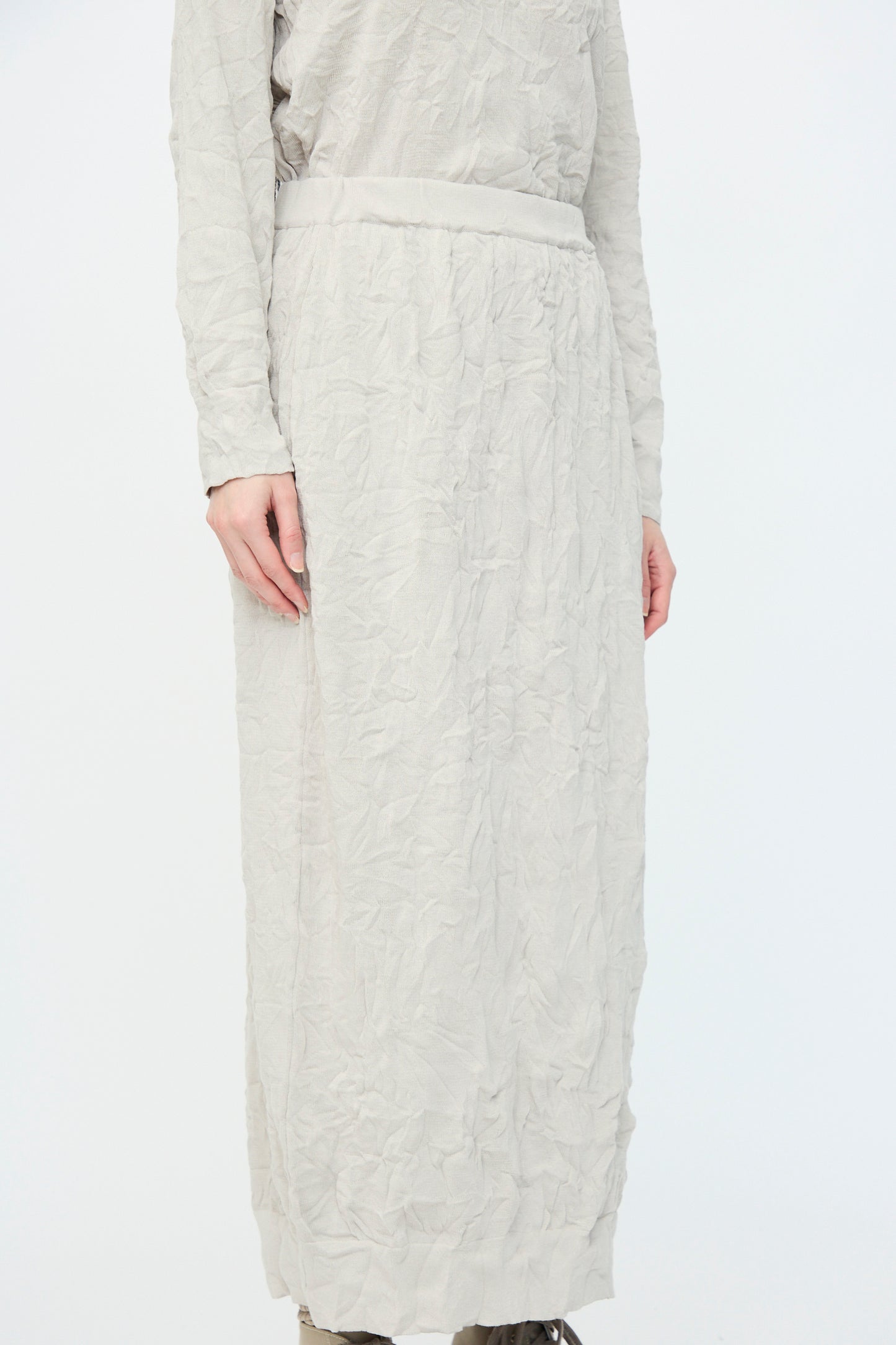 Person wearing a Crinkled Knit Skirt in Platinum by Black Crane with brown shoes against a plain background.