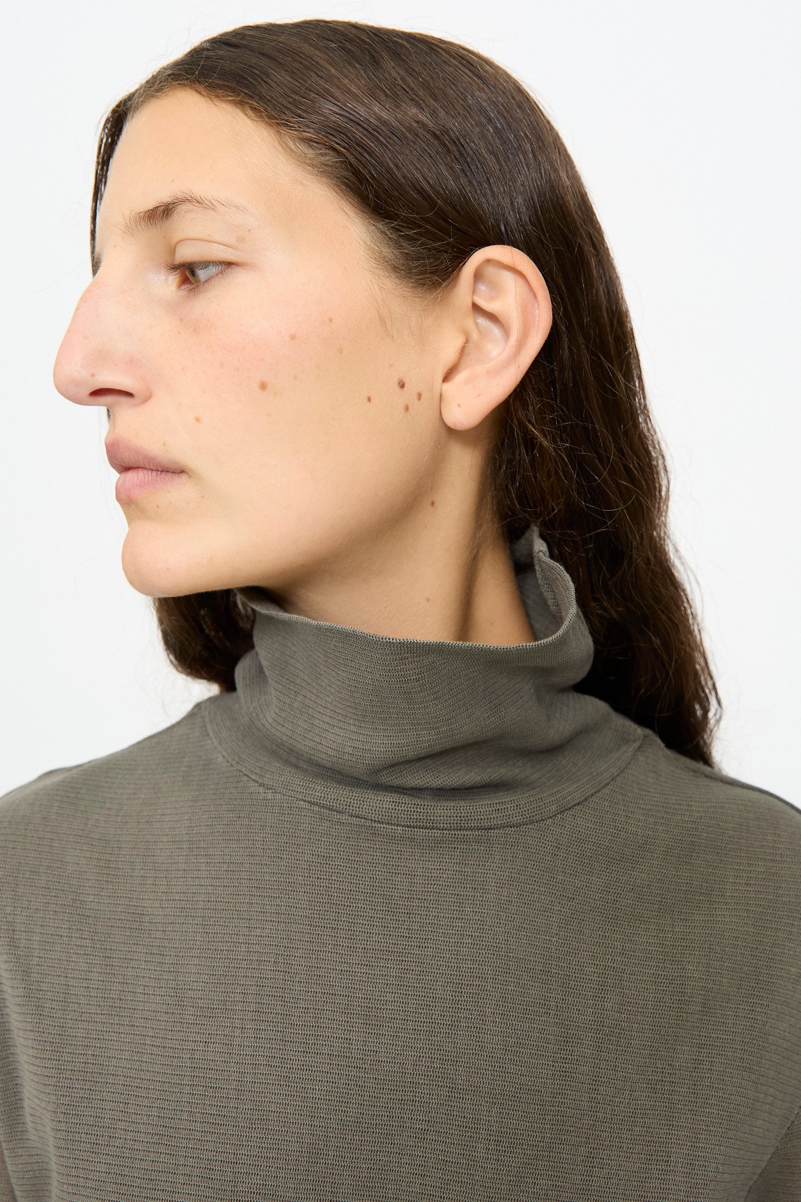 A person with long brown hair wears the Black Crane Double Mesh Turtleneck in Dark Stone, looking to the left against a plain white background.