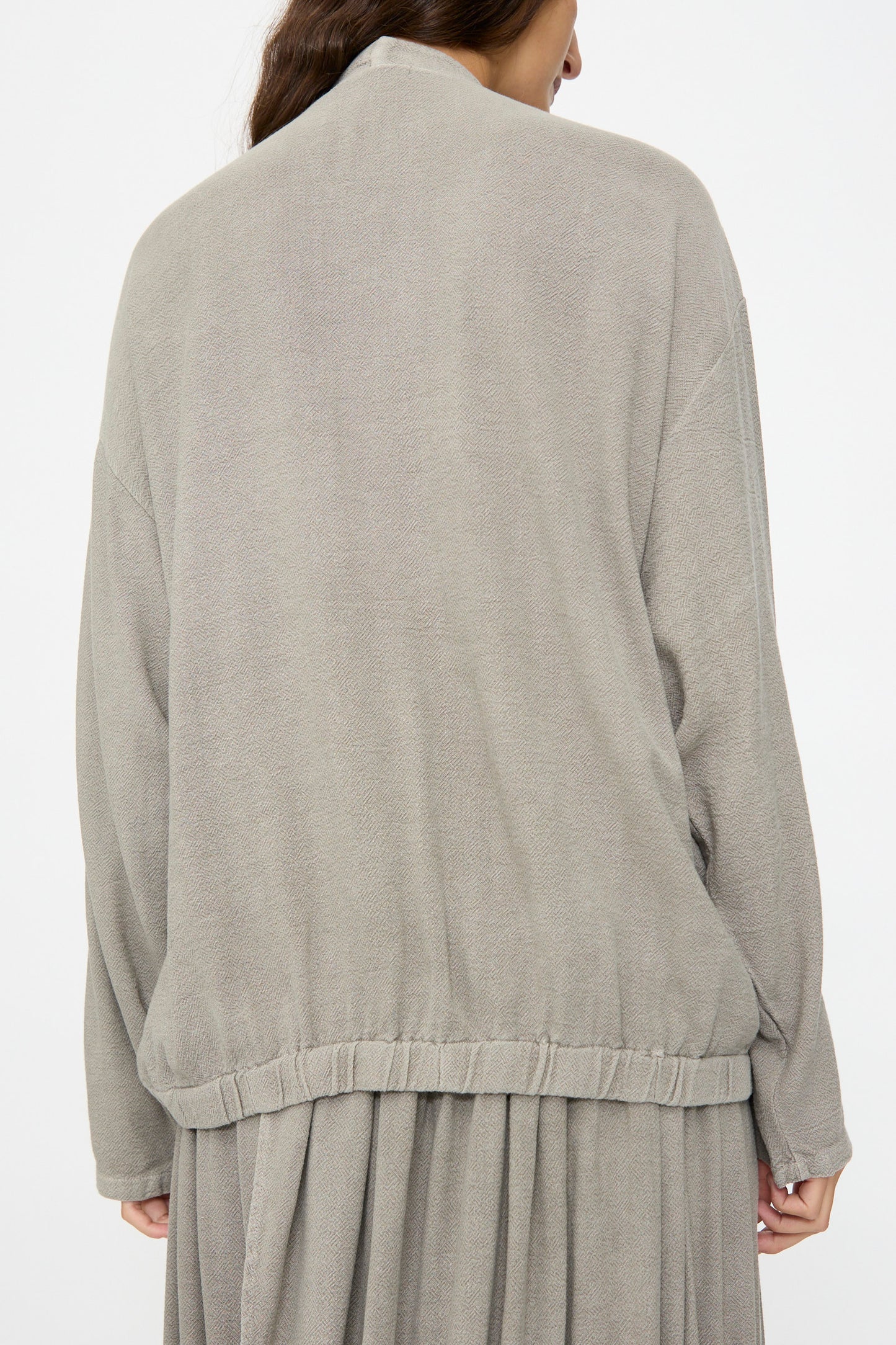 A person shown from the back wears the Black Crane Drapy Shirt in Dark Stone, paired with a matching skirt, against a plain white background.