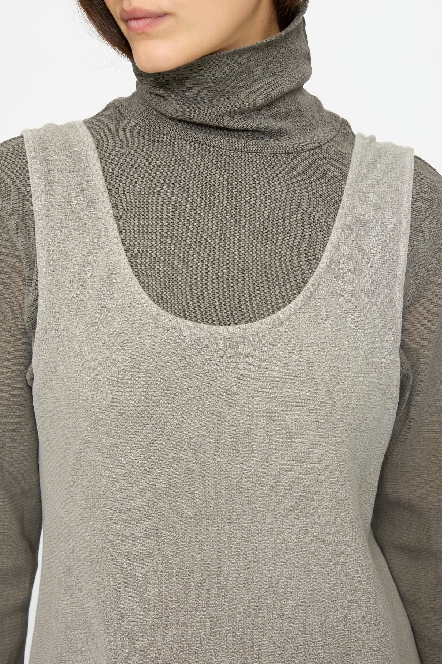 A person wearing Black Crane's Maxi Dress in Dark Stone, layered over a grey turtleneck top; shown from shoulders to upper chest.