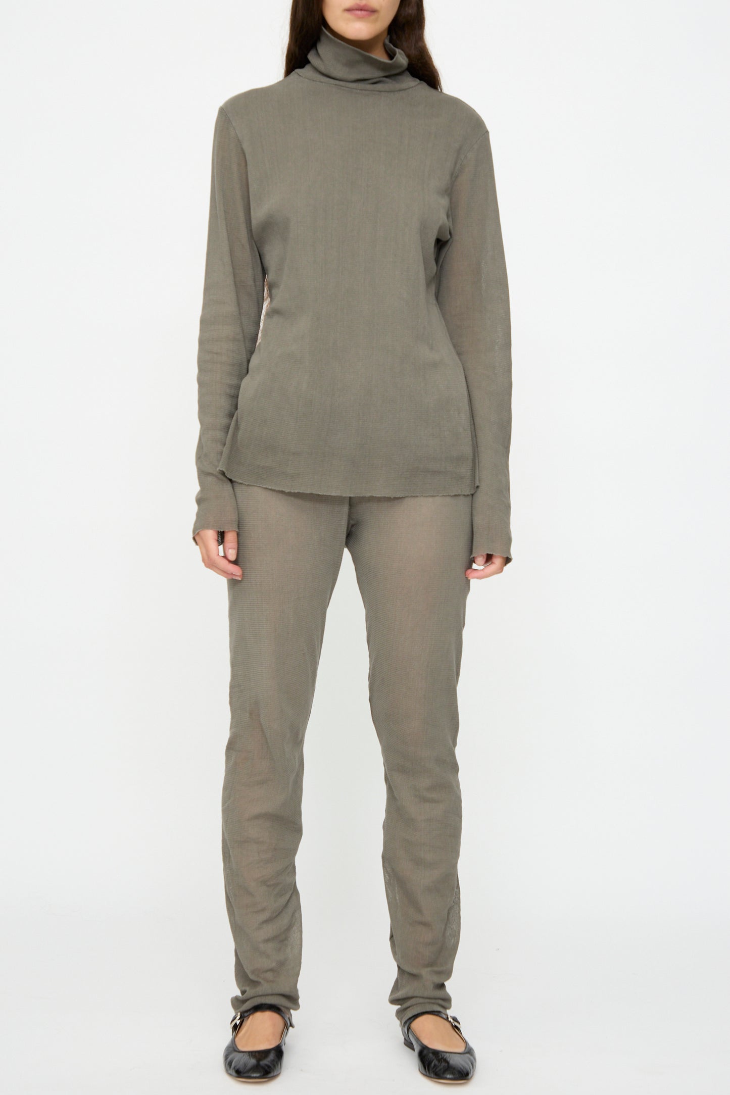 A person wears Black Crane's Mesh Leggings in Dark Stone with a matching taupe turtleneck, long sleeves, and black ballet flats, standing against a plain white background.