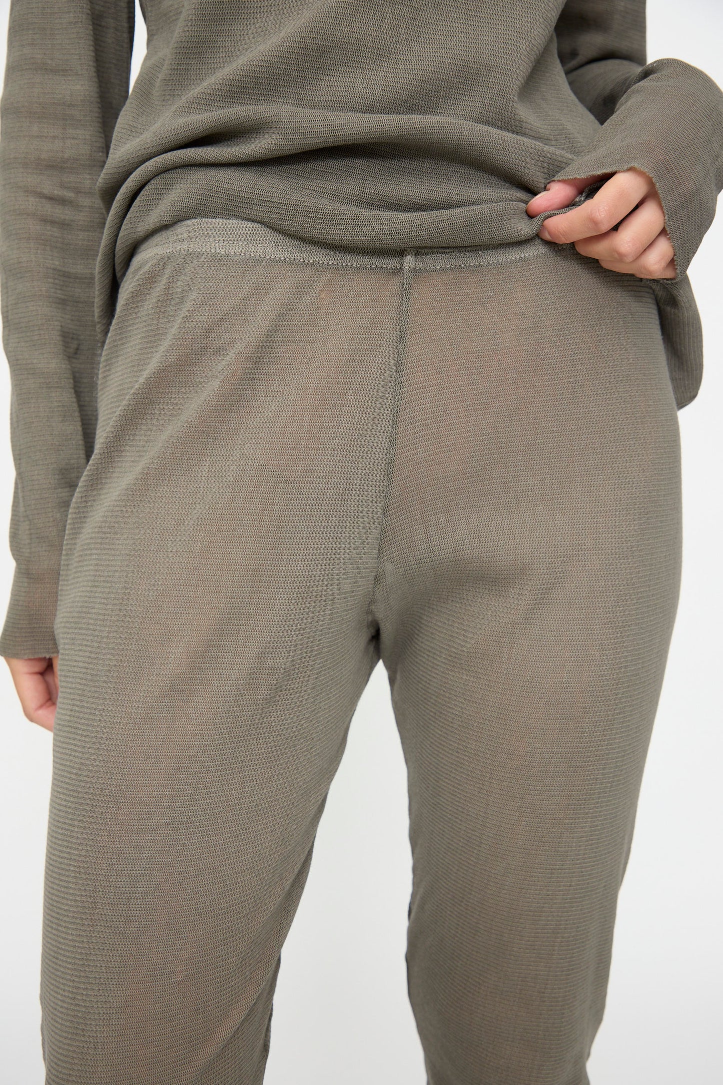 Person wearing Black Crane Mesh Leggings in Dark Stone, holding the shirt hem up with one hand against a plain background.