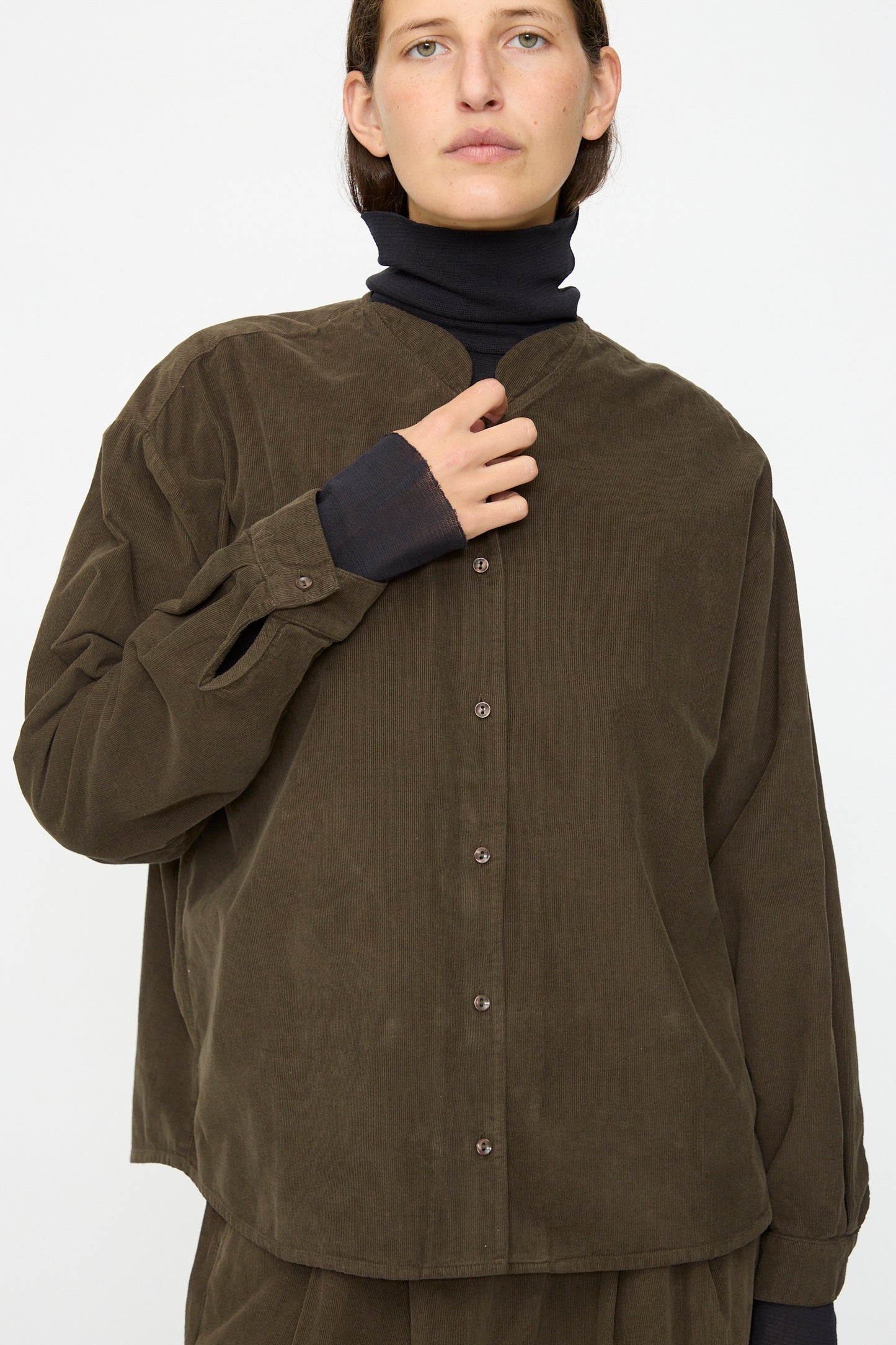 Model wears the Black Crane Nehru Shirt in Dark Forest, styled loosely over a black turtleneck, set against a plain light background.