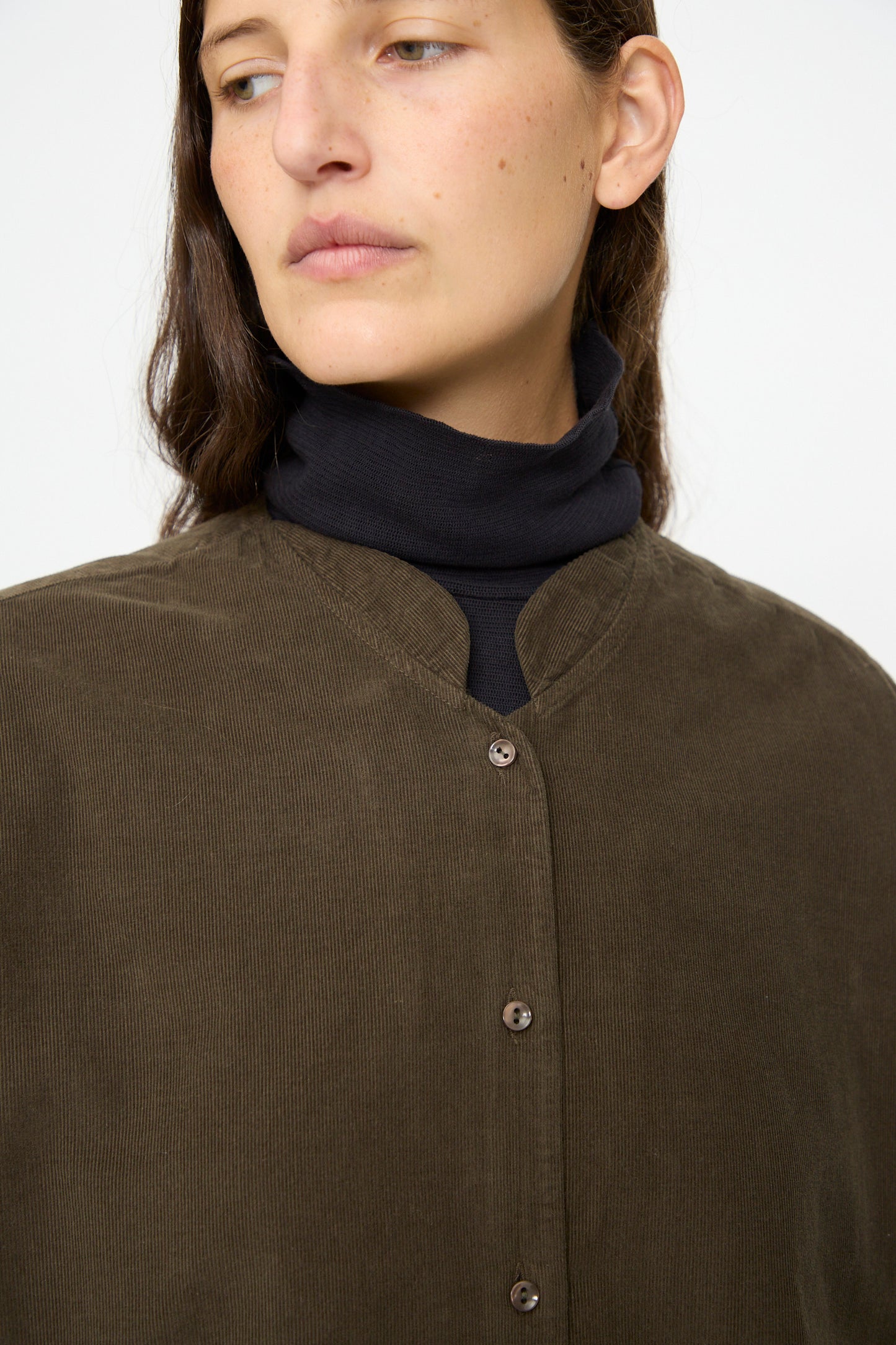 A person wears the Black Crane Nehru Shirt in Dark Forest over a black turtleneck, gazing slightly to the side against a plain background.