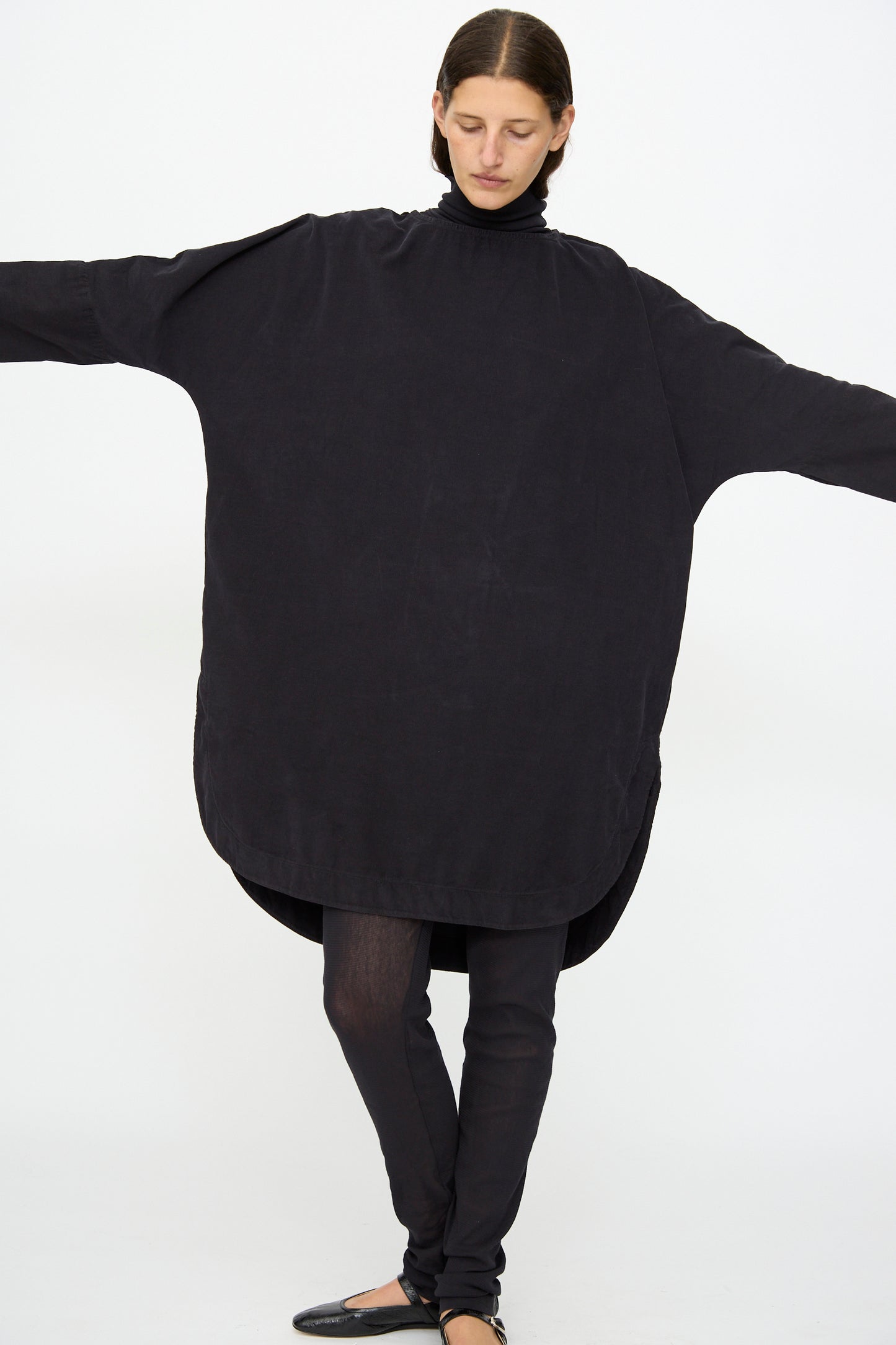 A person wears the Black Crane Painter Dress in Dark Navy, styled as a loose, oversized tunic with black leggings and shoes, standing with arms extended against a plain white background.