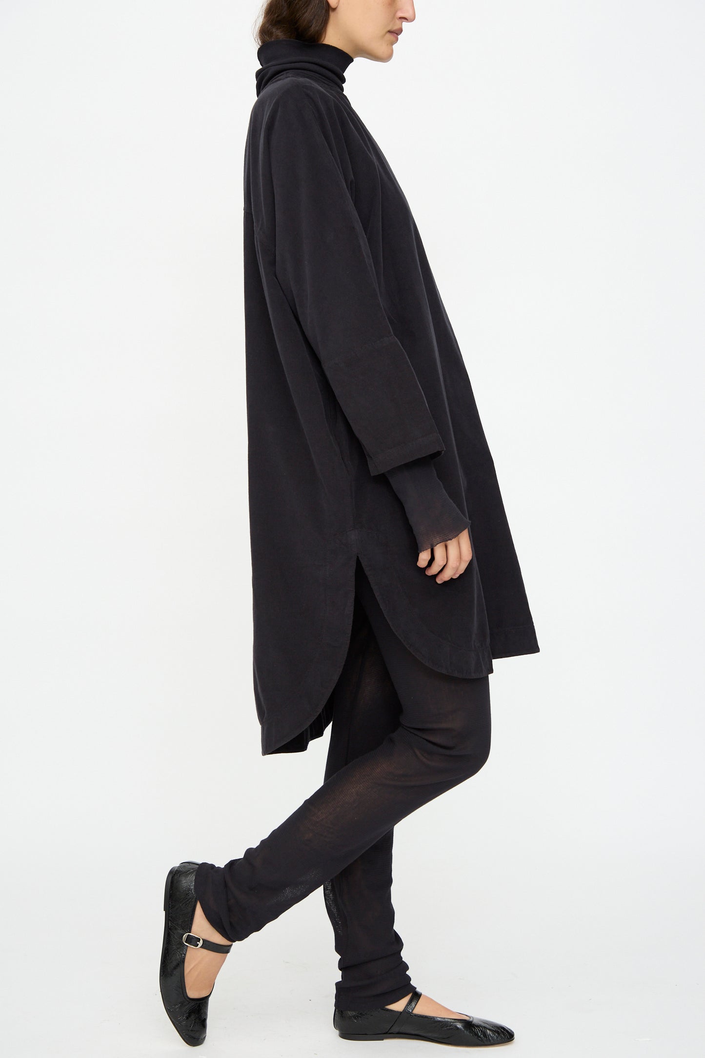 A person in the Black Crane Painter Dress in Dark Navy, paired with black leggings and ballet flats, stands sideways against a plain white background.