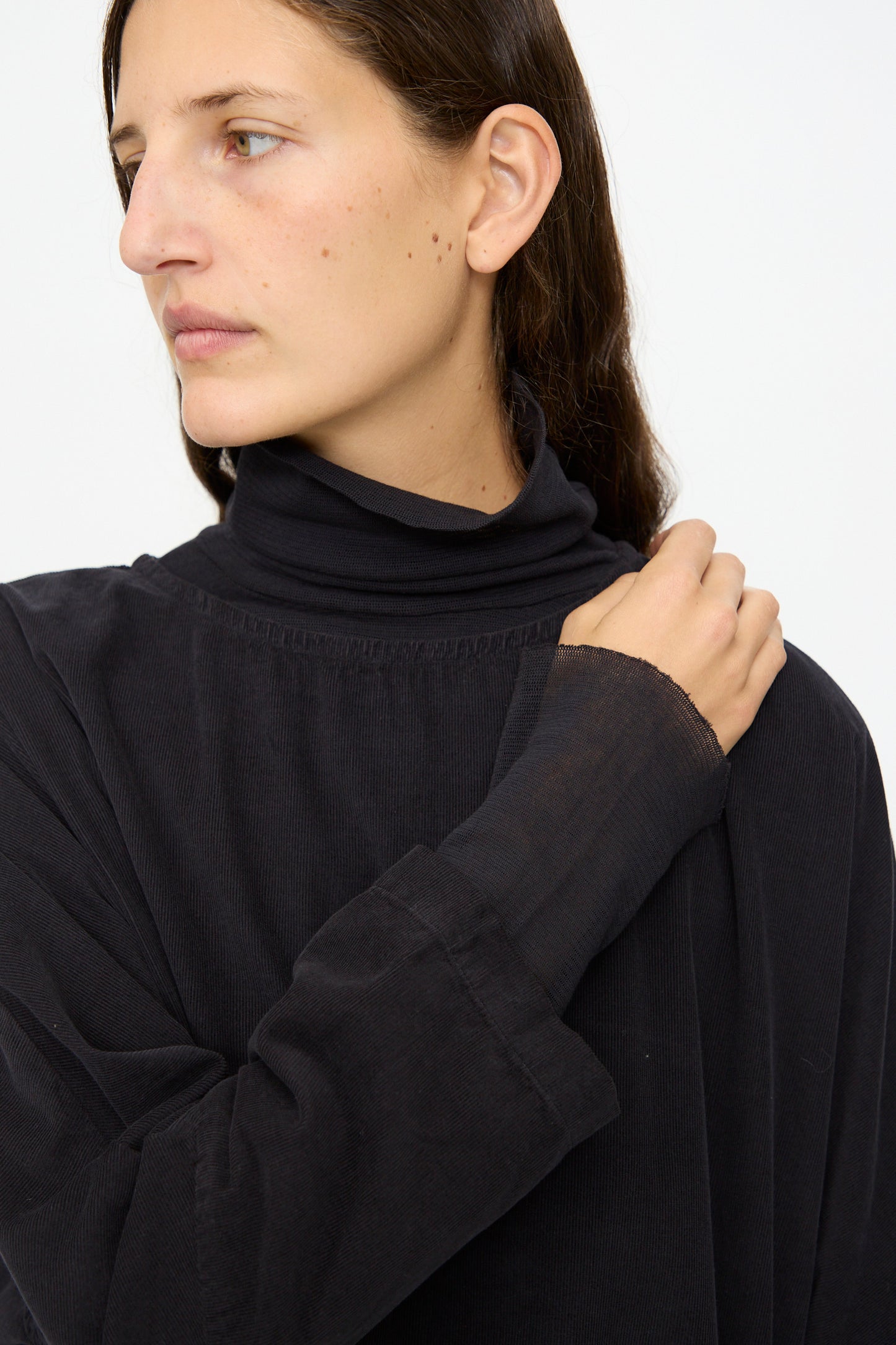 A person with long brown hair wears the Black Crane Painter Dress in Dark Navy, looking to the side with one hand on their shoulder against a plain light background.