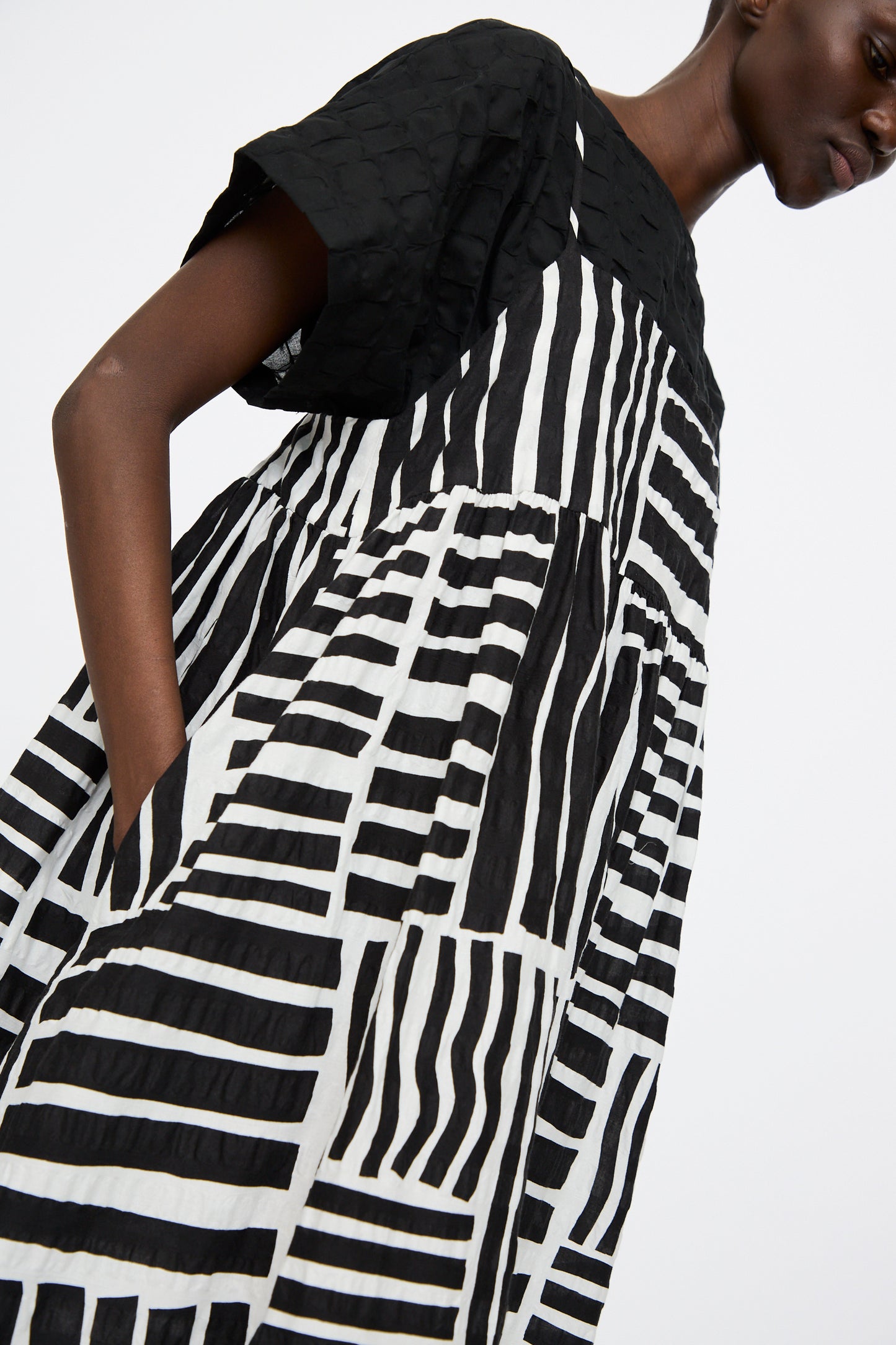 Model wears Black Crane's Strap Dress in Black Print—a loose, sleeveless midi dress in Japanese cotton with a bold black and white graphic pattern—layered over a short-sleeved black top.