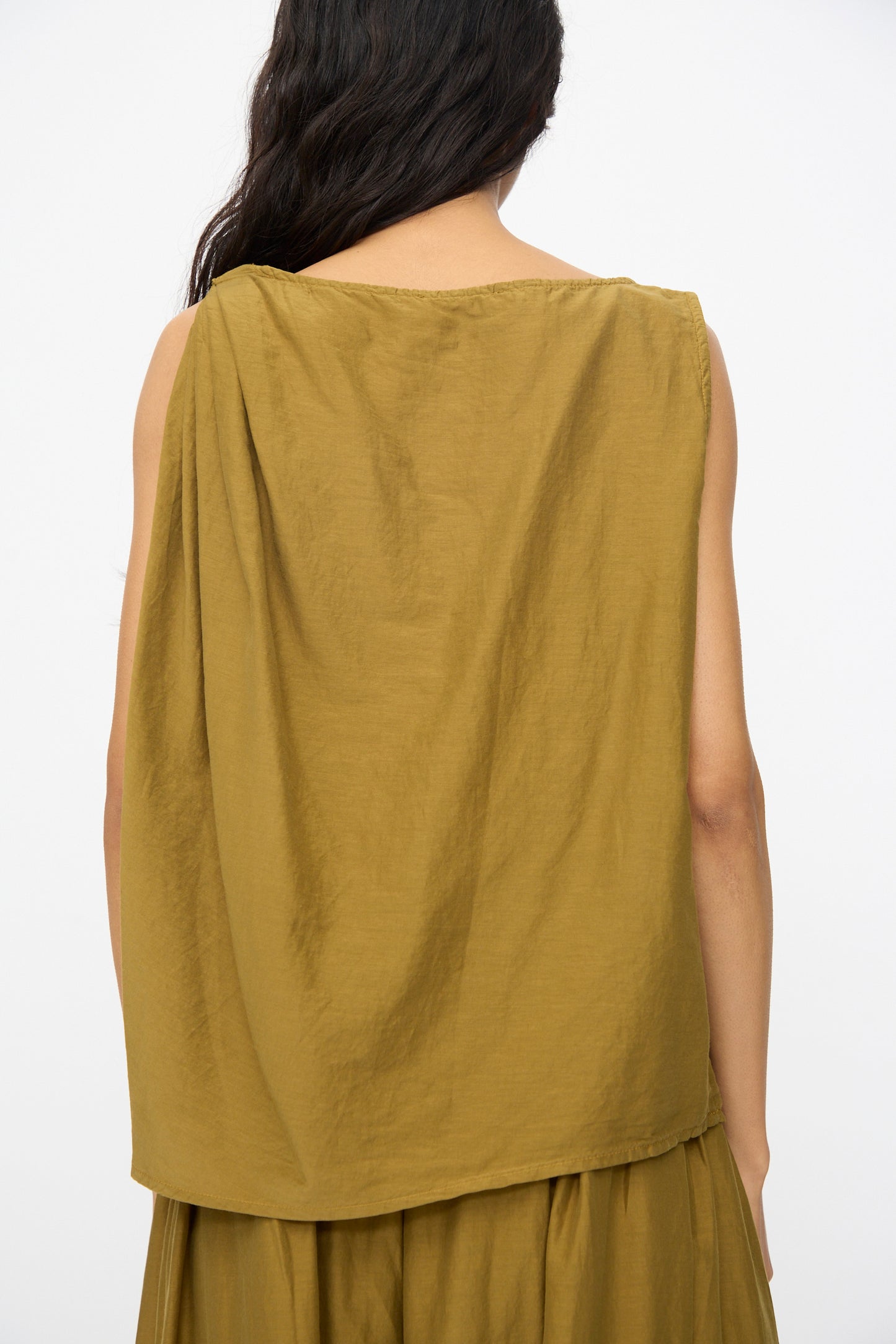 A person with long dark hair is shown from the back, wearing Black Crane's Twisted Tank Top in Dark Olive paired with a matching skirt.