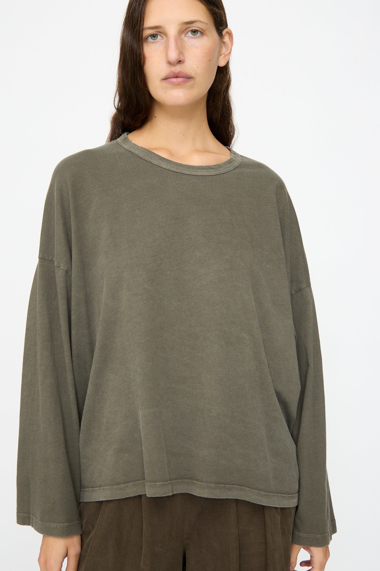 A person with long brown hair wears the Black Crane Wide Long Sleeve Tee in Slate and brown pants against a plain white background.