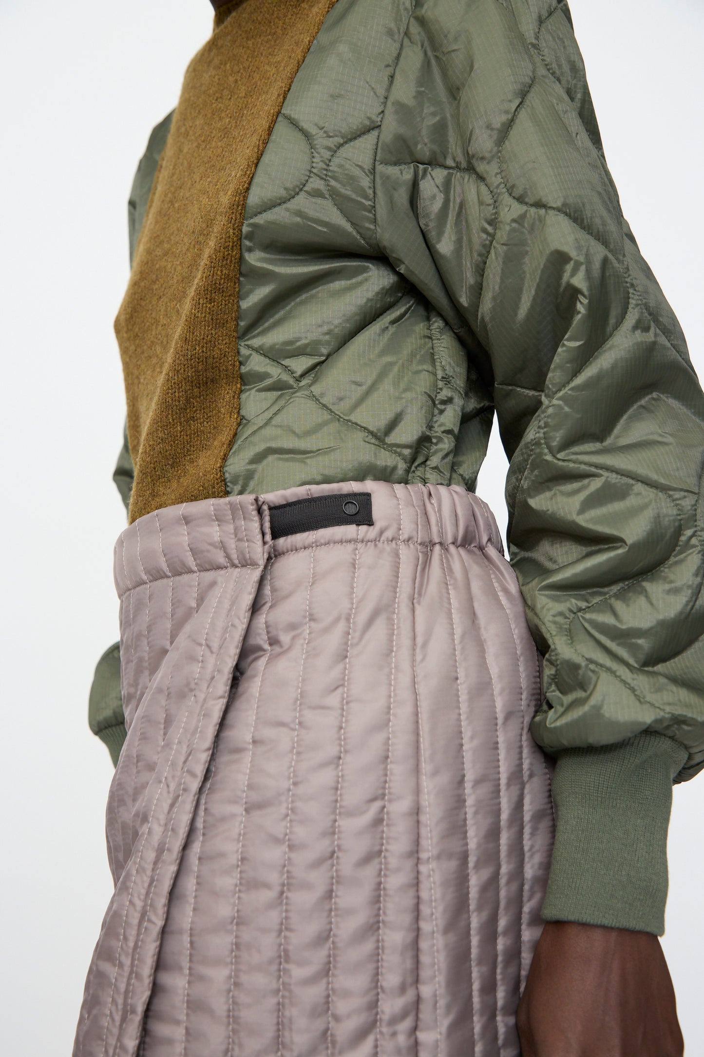A person wears an olive green, quilted long-sleeve top and the Bless No. 08 Monpe Skirt in Beige, shown from torso to mid-thigh against a plain background.